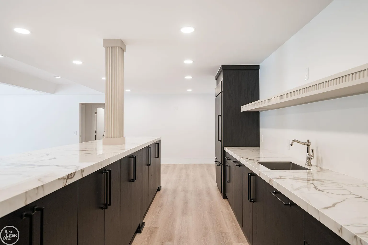 Dark cabinetry contrasts against bright stone countertops, while extensive prep space, open shelving, integrated refrigeration, and a sink allow the area to function like a secondary kitchen. 