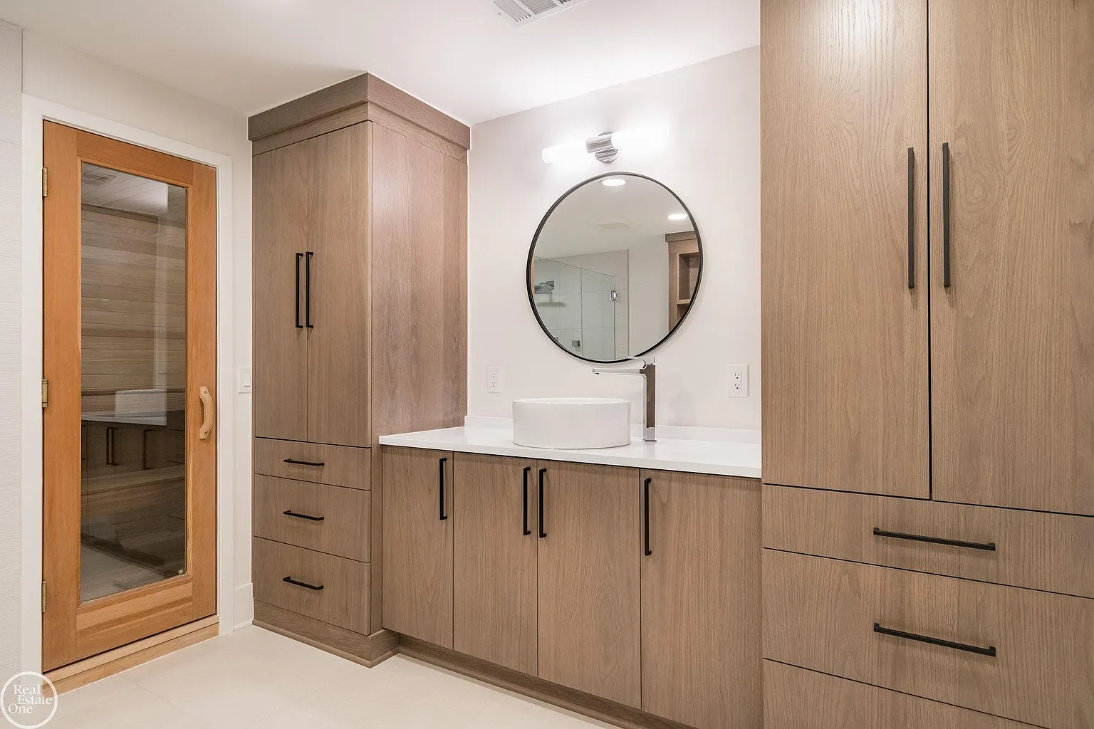 The sauna is enclosed in warm wood paneling next to light wood vanity.