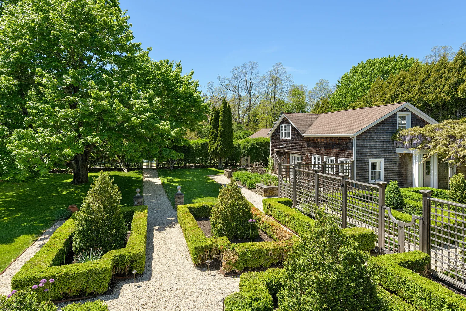 The walk to the front entrance begins along a gravel pathway lined with meticulously clipped boxwood hedges and geometric garden beds.