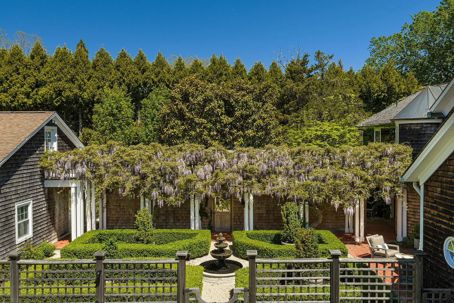 Closer to the home, a central fountain sits within a courtyard garden framed by sculpted hedges, while a pergola draped in cascading wisteria connects the various wings of the residence. 