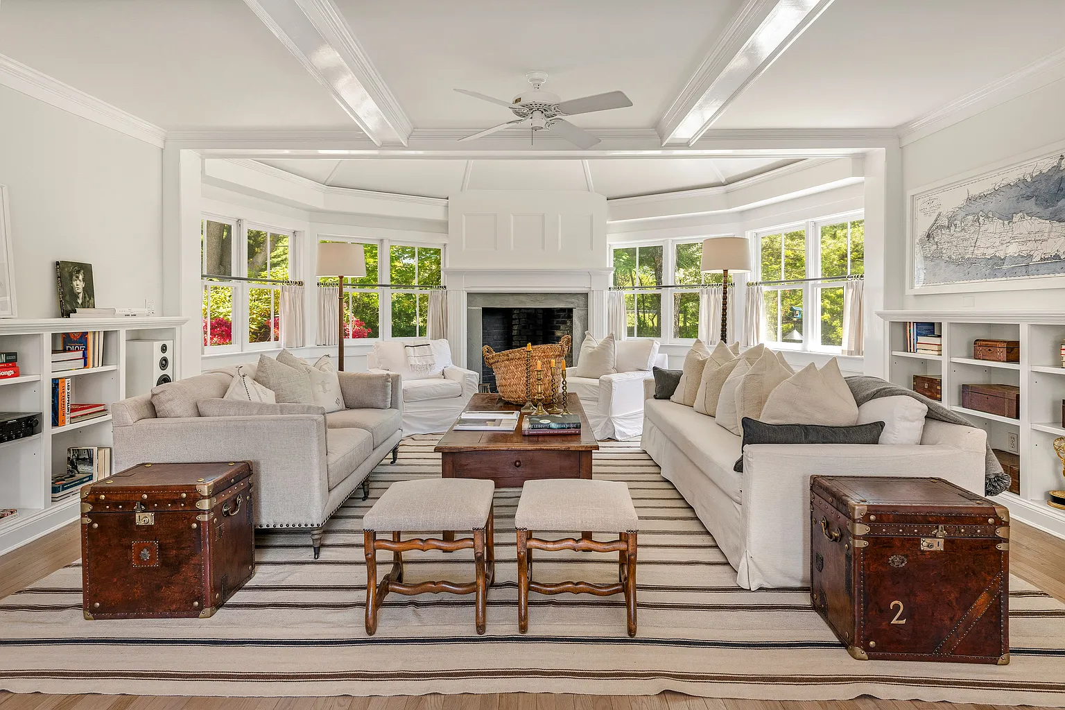 One seating area is arranged around a substantial stone fireplace set within a window-lined alcove. 