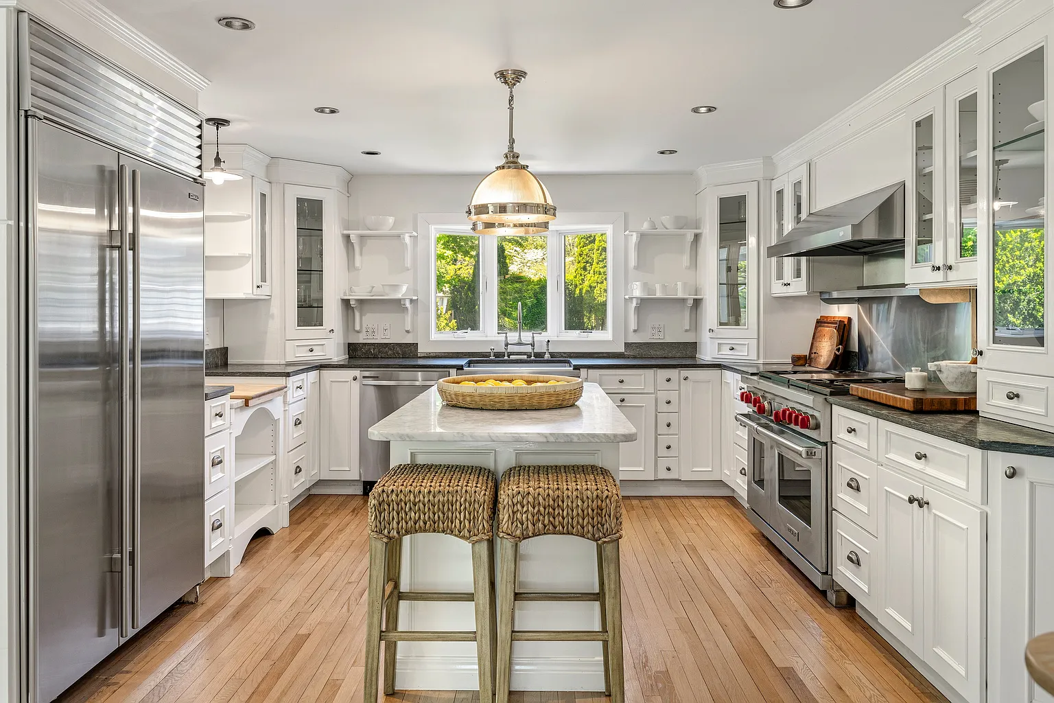The kitchen features white custom cabinetry, glass-front upper cabinets, open display shelving, and polished stone countertops, creating a bright, clean aesthetic.