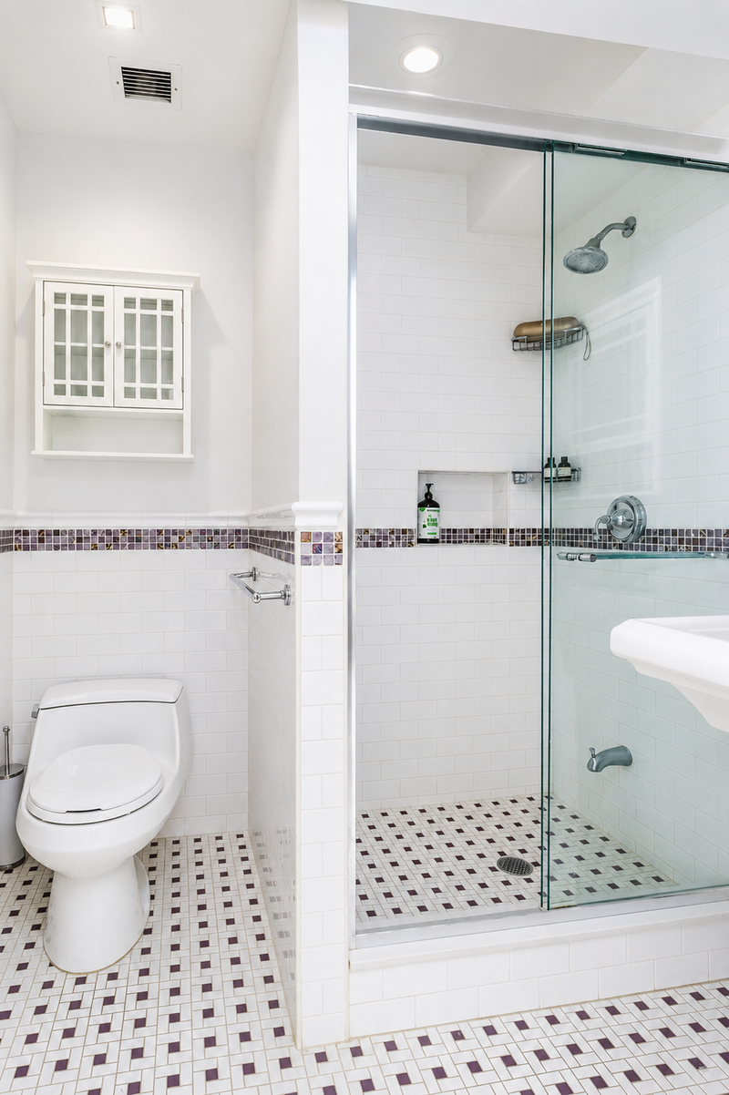 White subway tile wraps the walls of the oversized walk-in shower, while a mosaic accent band and matching patterned floor tile introduce subtle contrast and texture.