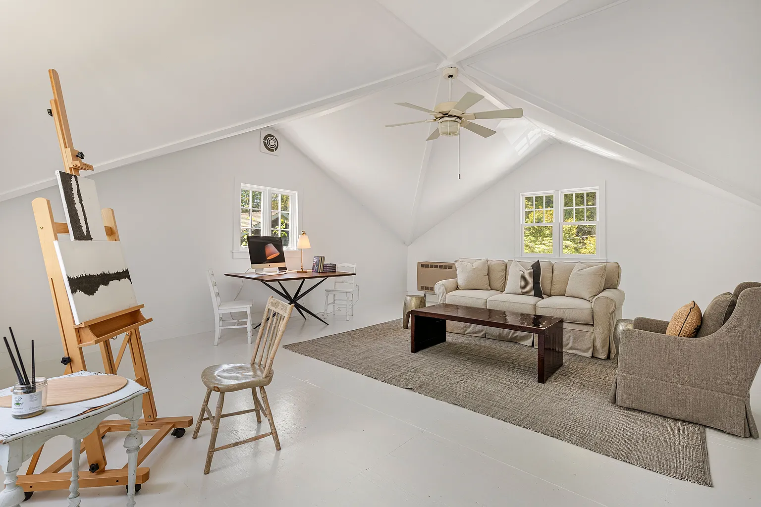 White-painted floors and walls create a clean backdrop, while windows on multiple sides bring in natural light and views of the surrounding greenery.