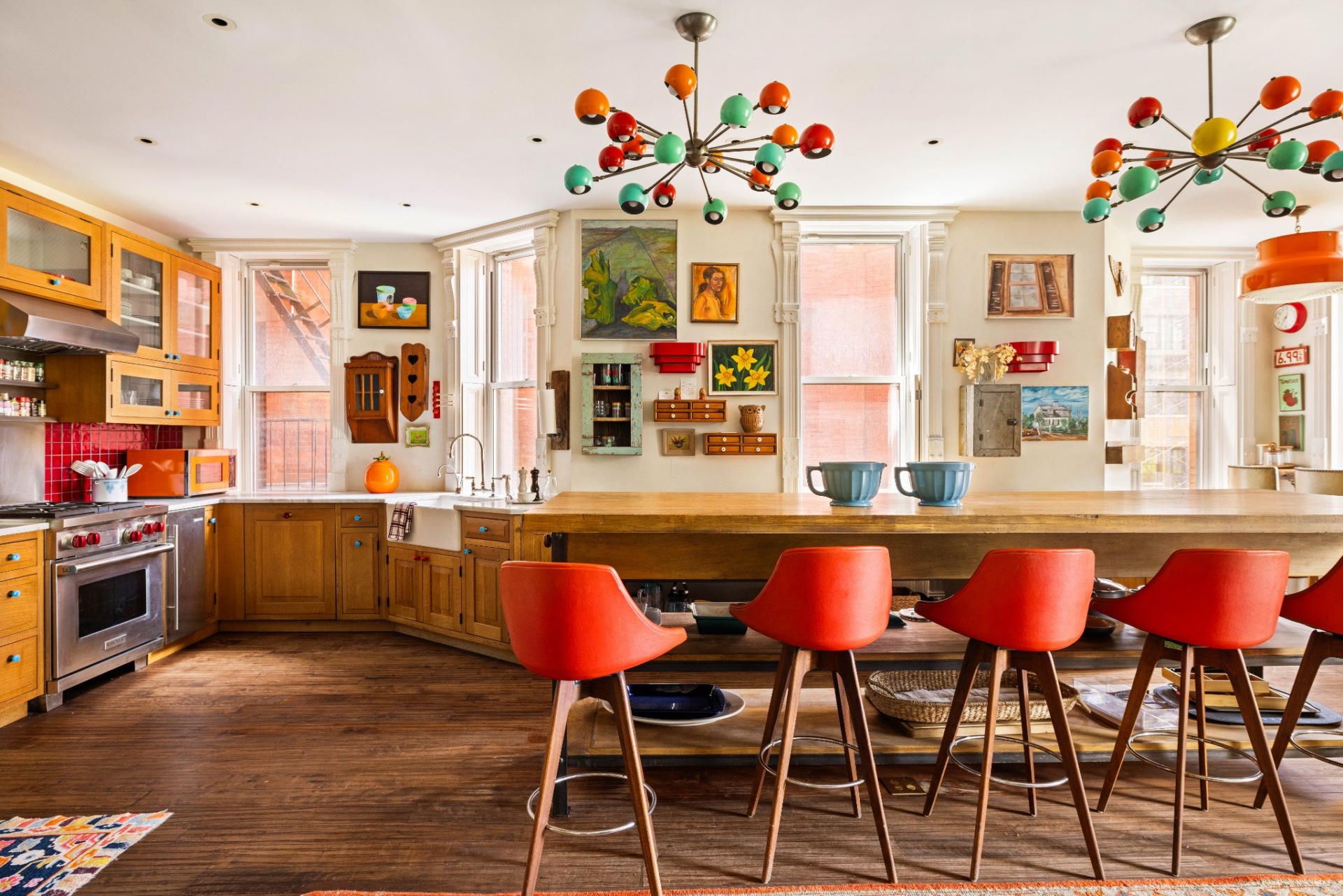 Positioned along a wall of oversized windows overlooking Gramercy Park, the room combines warm wood cabinetry, colorful vintage-inspired lighting, and an expansive central island.