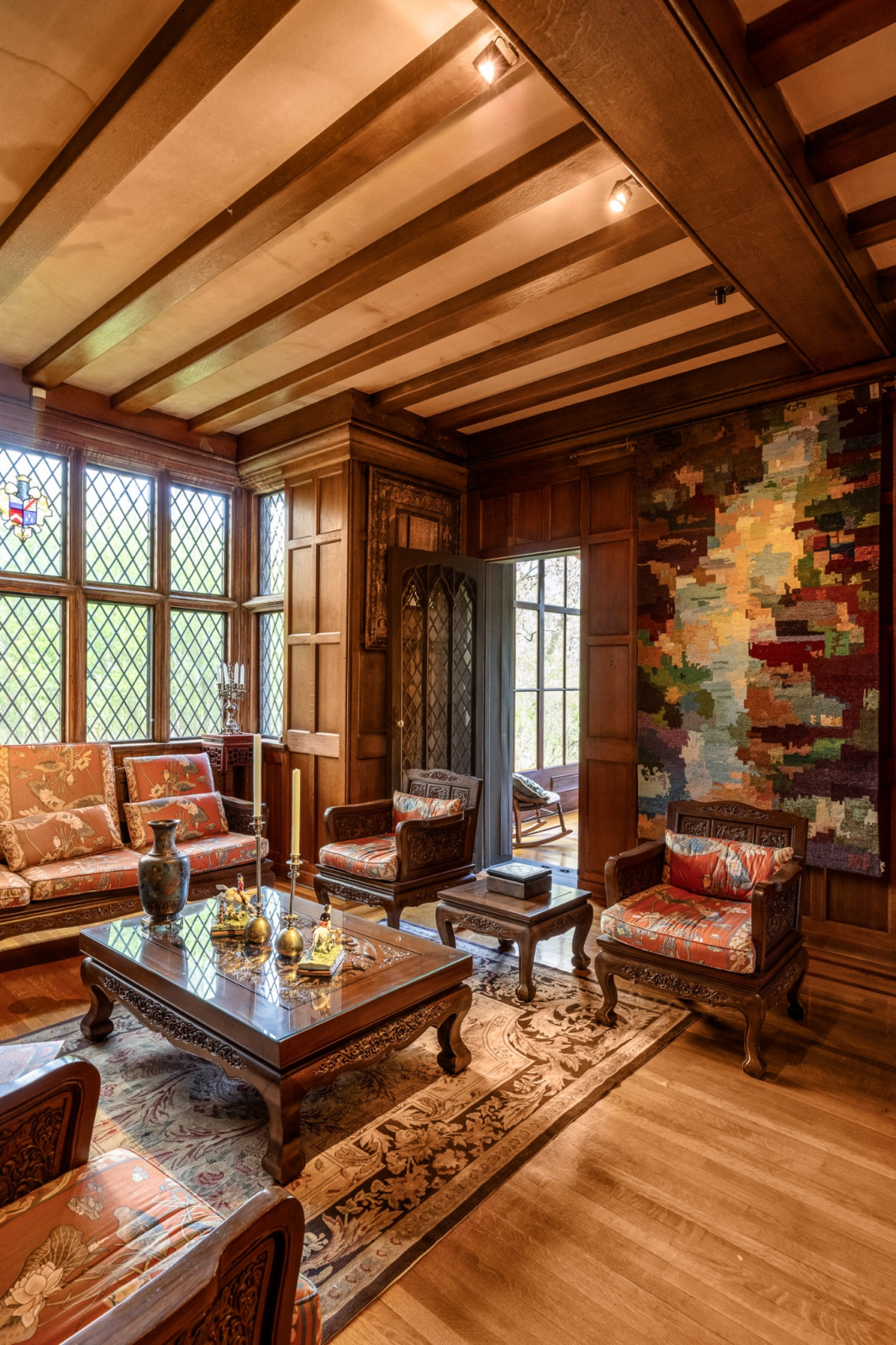 Carved wood furnishings, paneled walls, decorative millwork, and a coffered ceiling reinforce the home's Tudor character, while views into connected rooms emphasize the home's interconnected layout.
