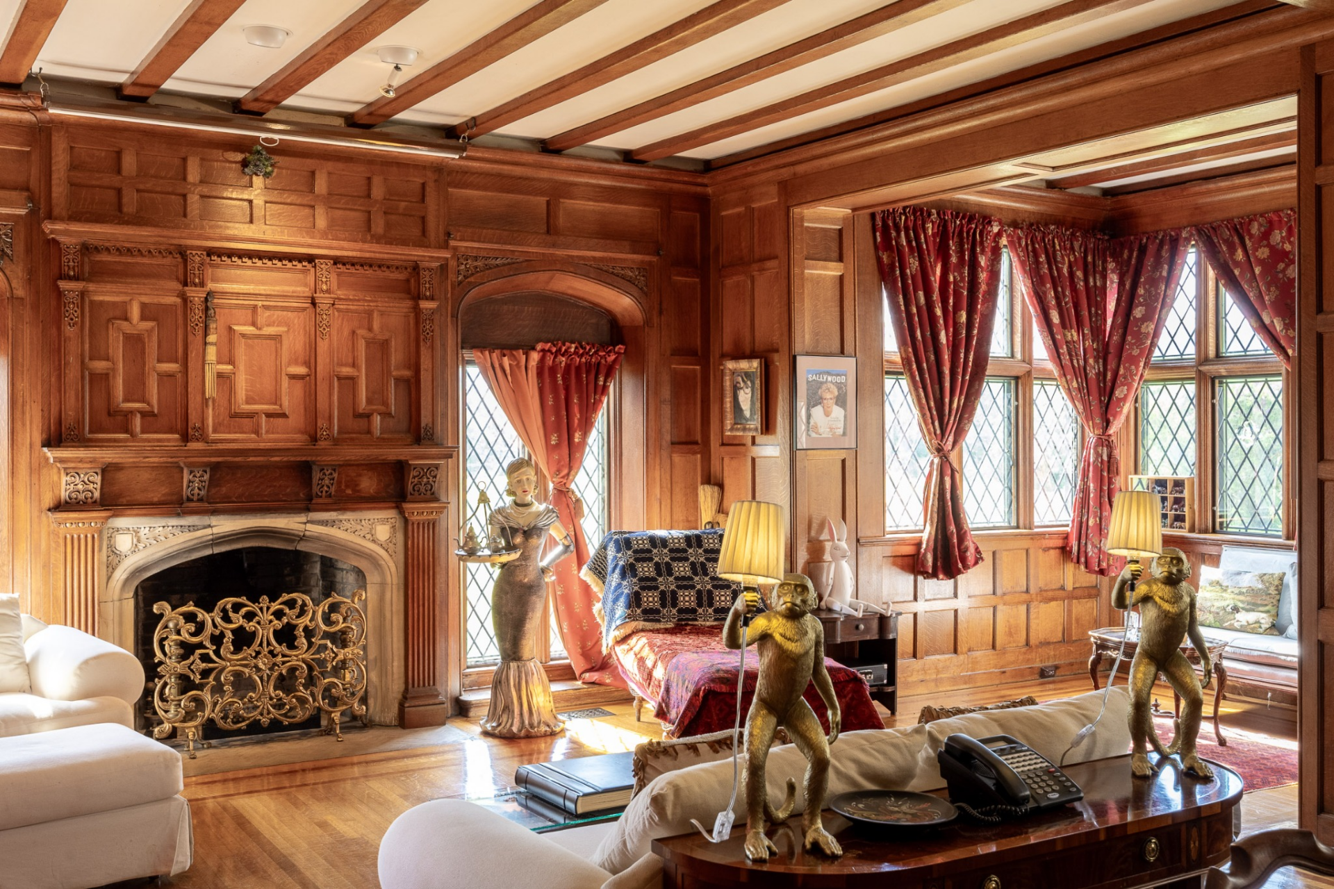 Just beyond, a larger living room offers a more relaxed setting with a carved stone fireplace set beneath elaborate woodwork, while window-lined seating areas bring in views of the surrounding grounds.