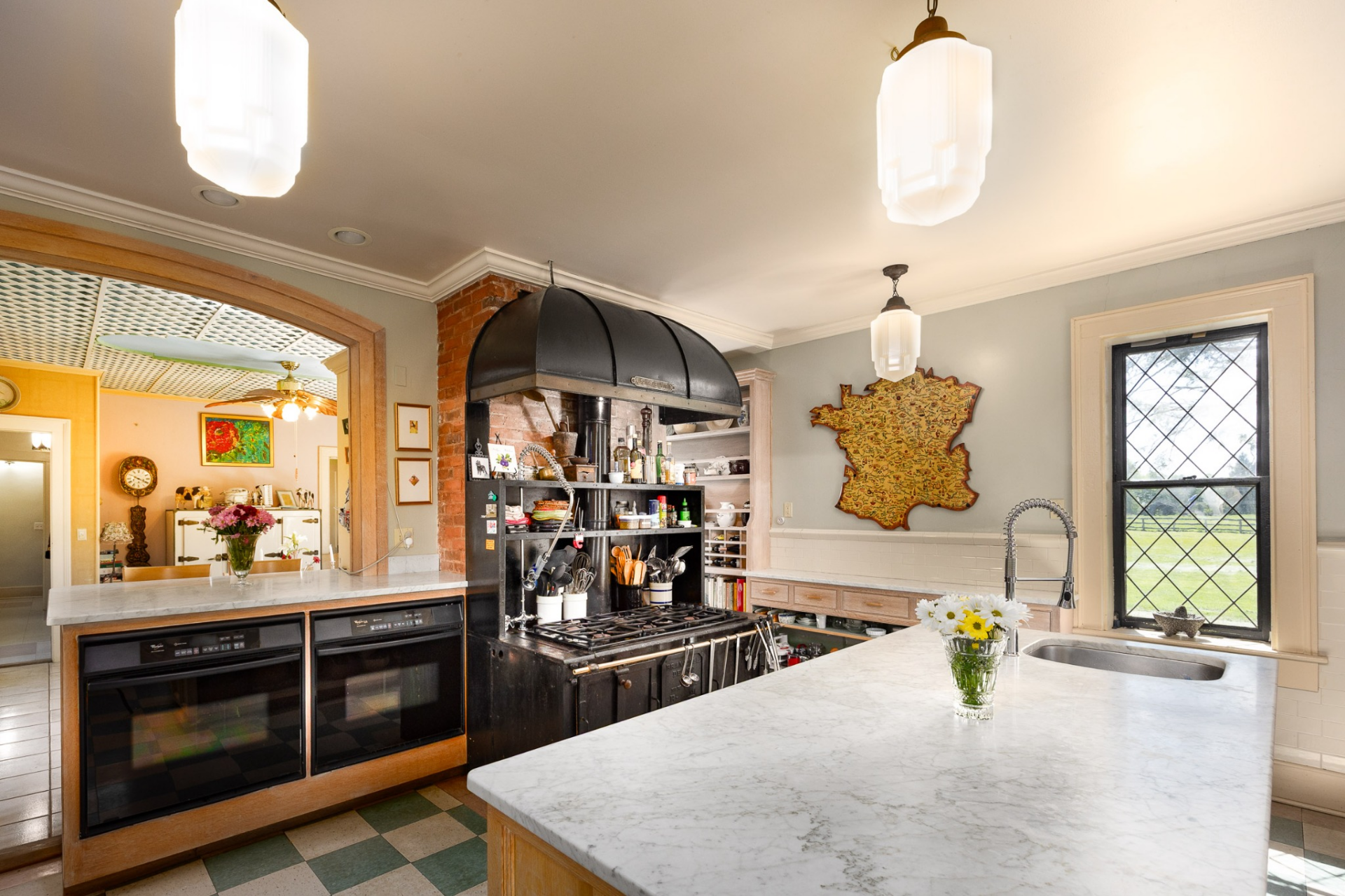 Balancing historic character with everyday functionality, the kitchen centers around a large marble-topped island and a black custom range hood set against exposed brick.