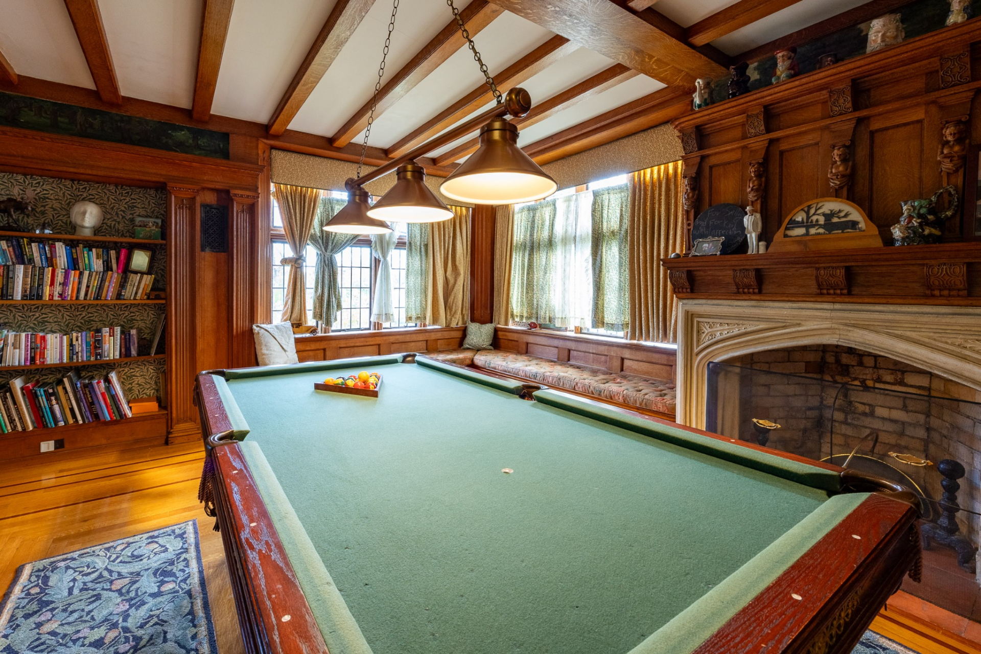The billiards lounge centers around a full-size pool table surrounded by built-in bookshelves, window seats, and a carved stone fireplace.