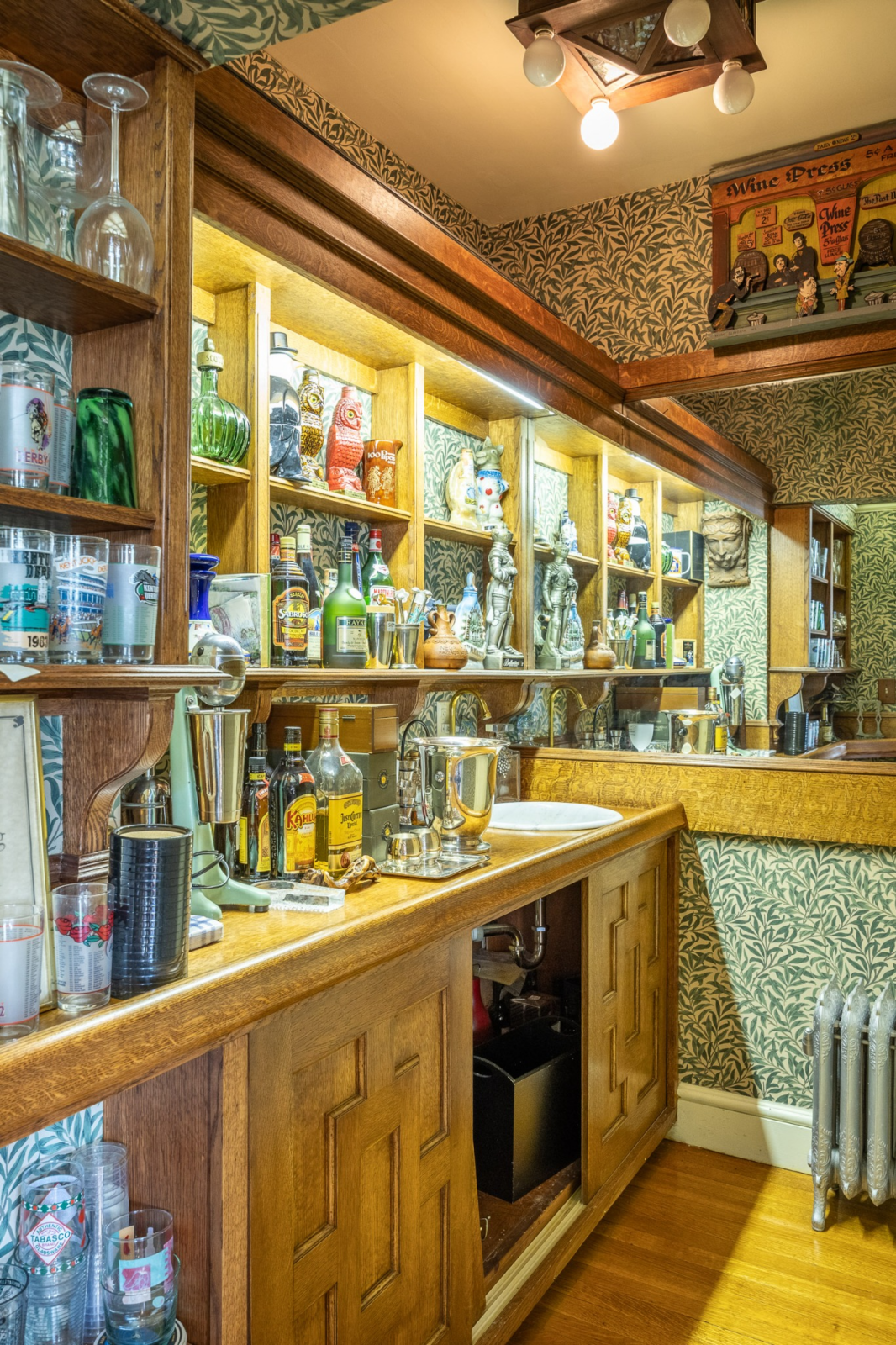 Nearby, a compact bar is lined with illuminated display shelving, mirrored walls, and patterned wallpaper that provide storage and display space for glassware and spirits.