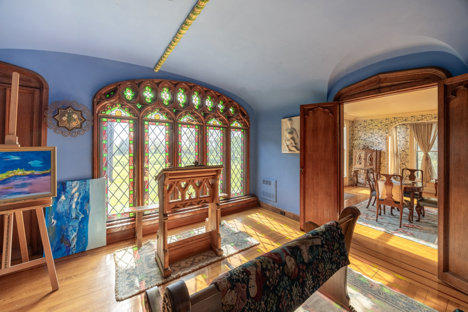 A striking stained-glass window framed by intricate Gothic-inspired woodwork fills the room with colored light, while a carved wooden lectern stands at its center. 