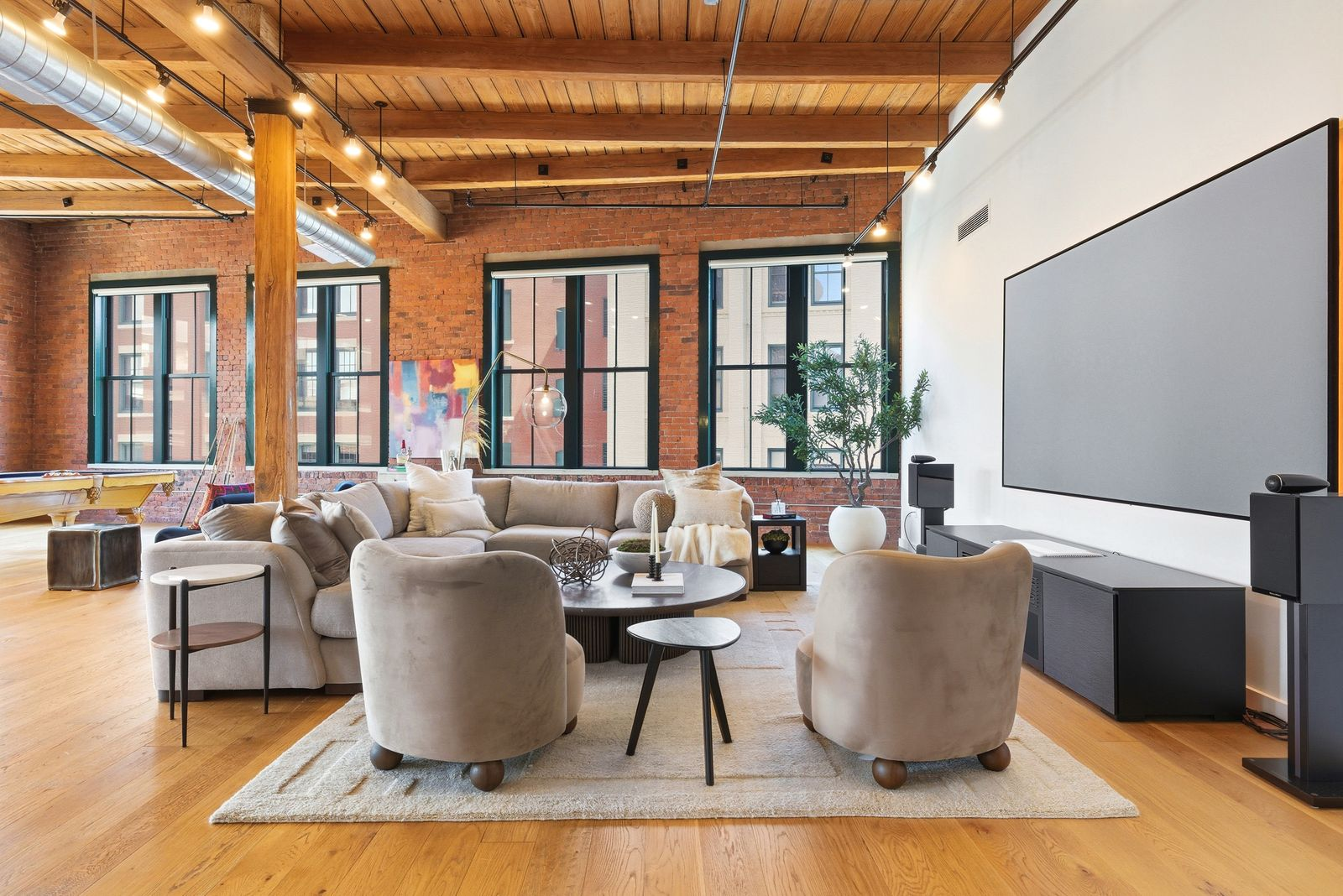 The open floor plan begins with a spacious living area arranged around a large sectional and a wall-mounted projection screen.
