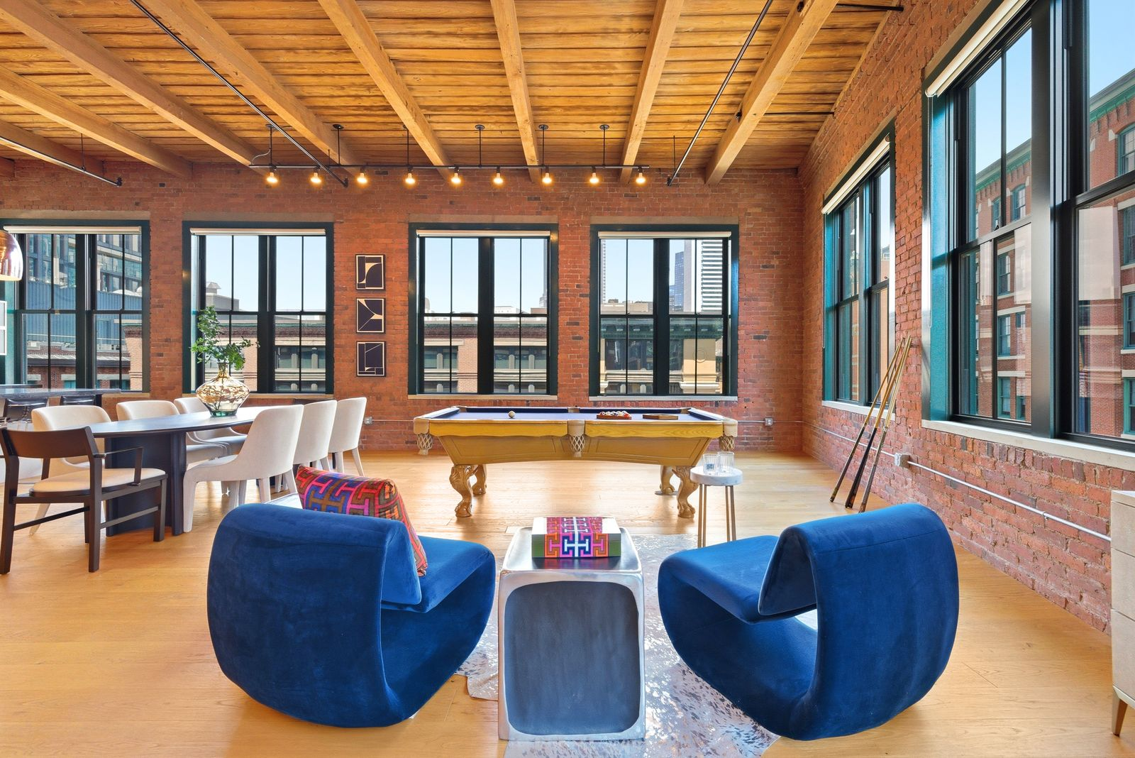 A classic pool table serves as the focal point along with two blue velvet chairs, creating a dedicated recreation zone within the larger open-concept layout.
