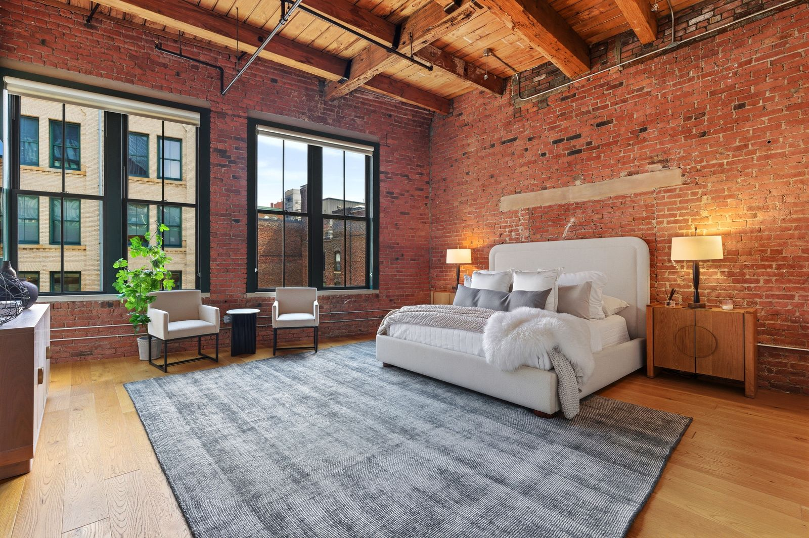 Stepping into the primary bedroom, the sleeping area is positioned toward the center of the room, leaving plenty of space around it for a sitting area near the windows.