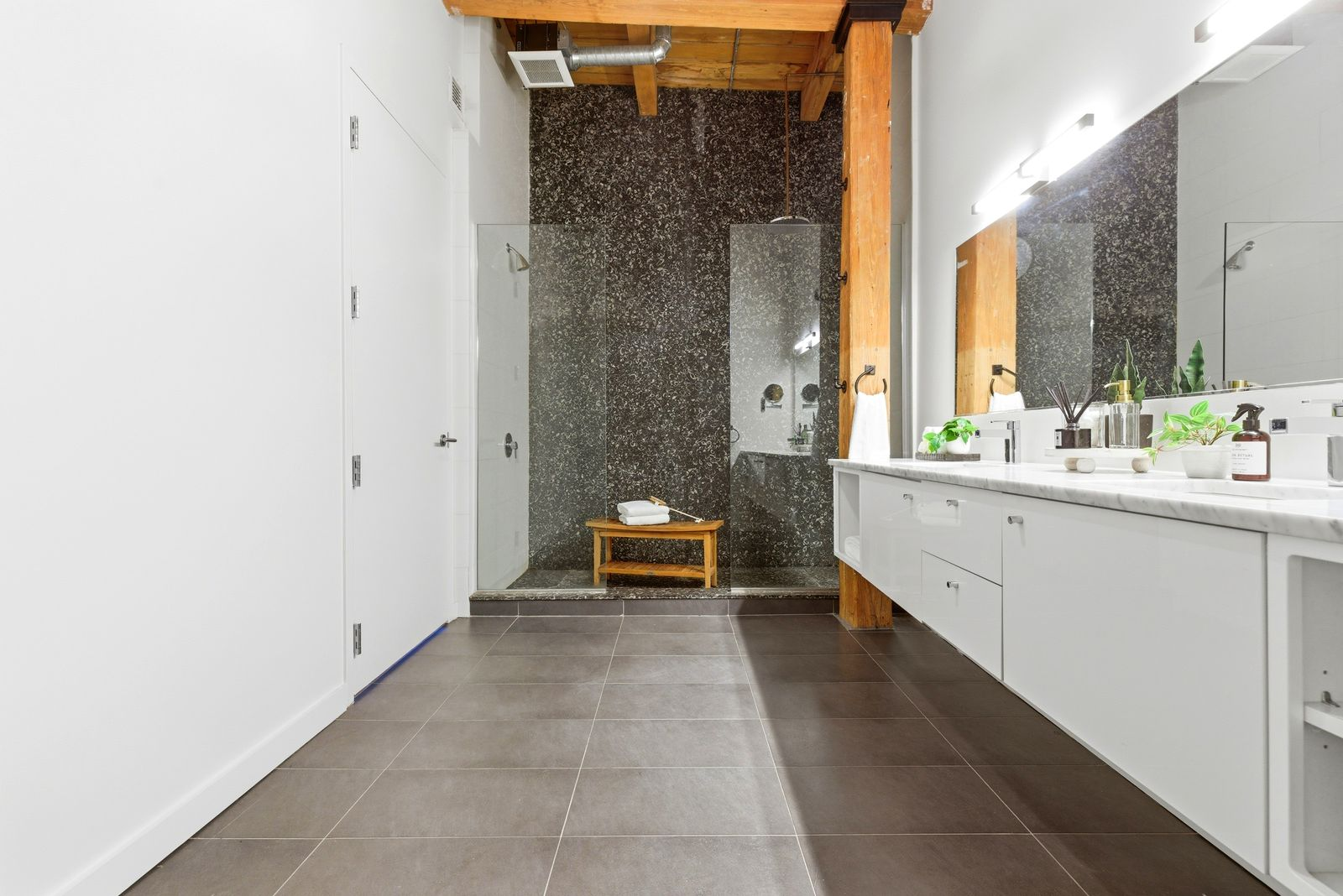 An expansive walk-in shower is enclosed in glass and finished with darker tile that contrasts with the bright palette found throughout the rest of the room.