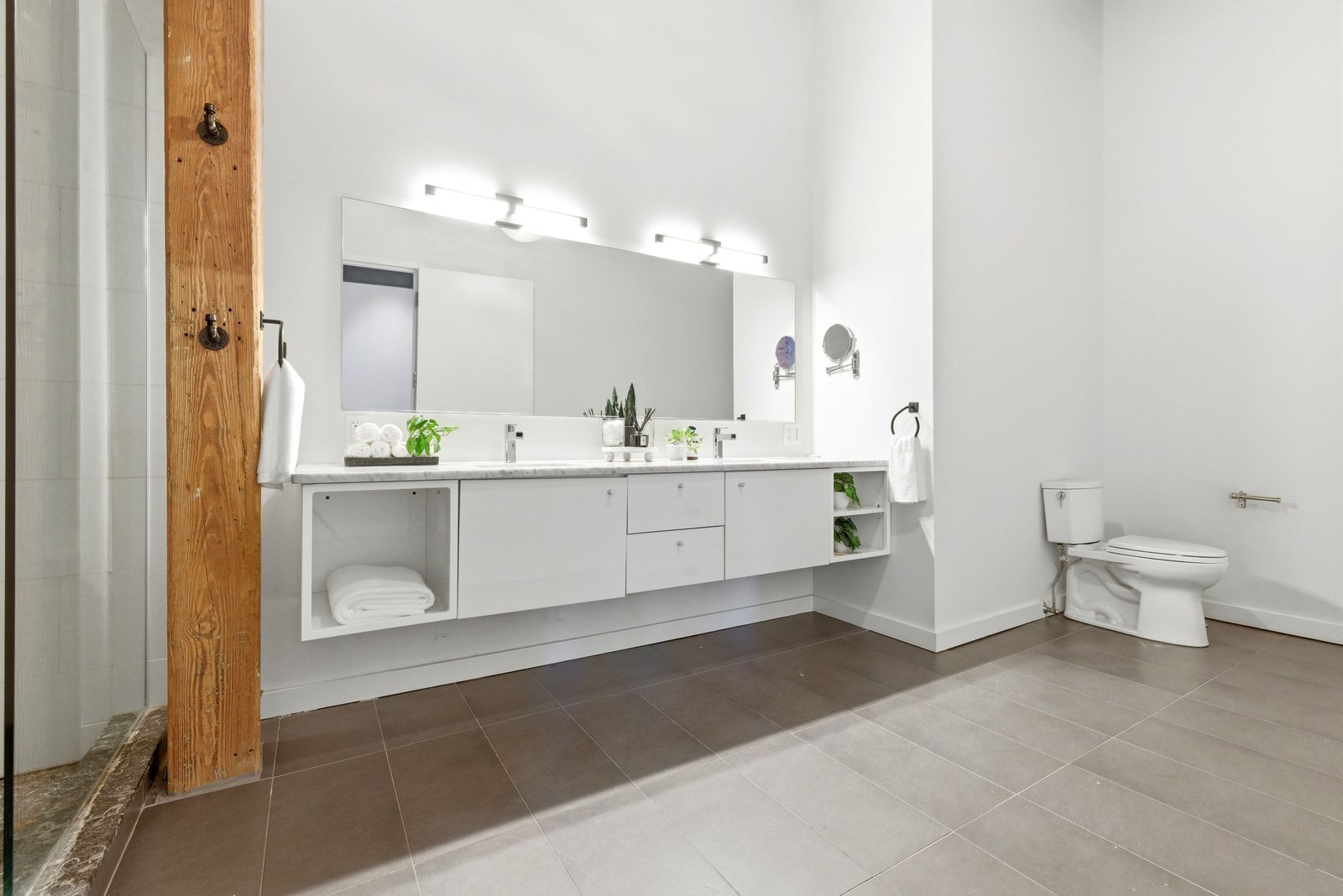 The en-suite bathroom has a more contemporary look with oversized tile flooring, crisp white walls, and a floating double vanity topped with stone countertops.