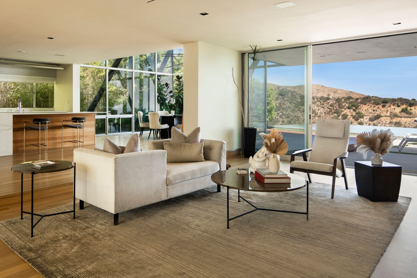 Floor-to-ceiling glass walls and wide sliding doors frame views of the surrounding hills while extending the space directly toward the backyard.