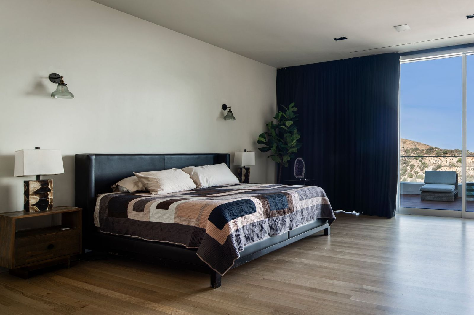 The room's generous space leaves plenty of room around the bed, while dark drapery frames the glass wall to make it easier to sleep with the bright city lights shining in the distance at night.