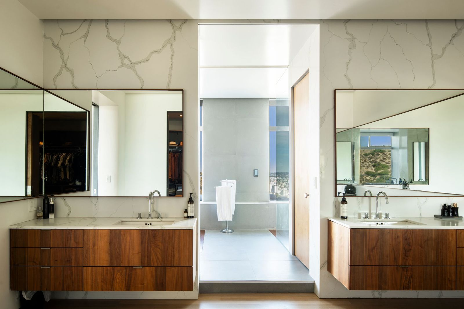 The en-suite bathroom continues the same modern design with floating walnut vanities positioned on opposite sides of the entrance.