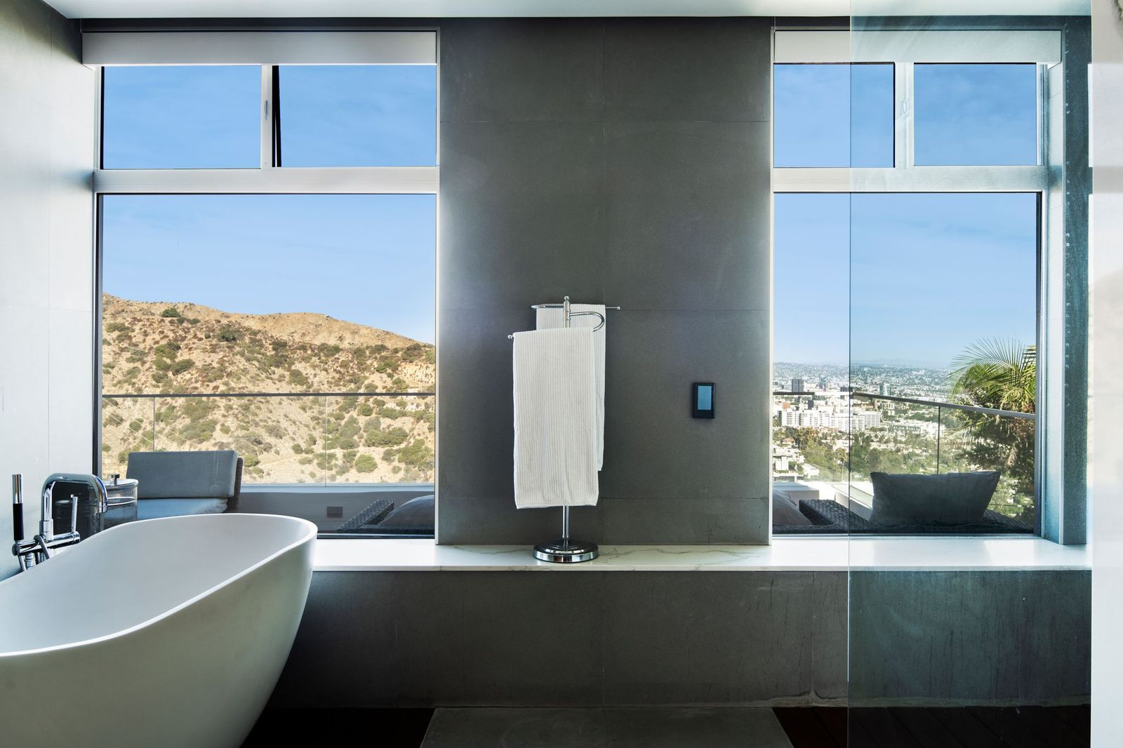 Beyond the vanities, the room opens to a soaking tub set beneath oversized picture windows that frame views of the hills and city.