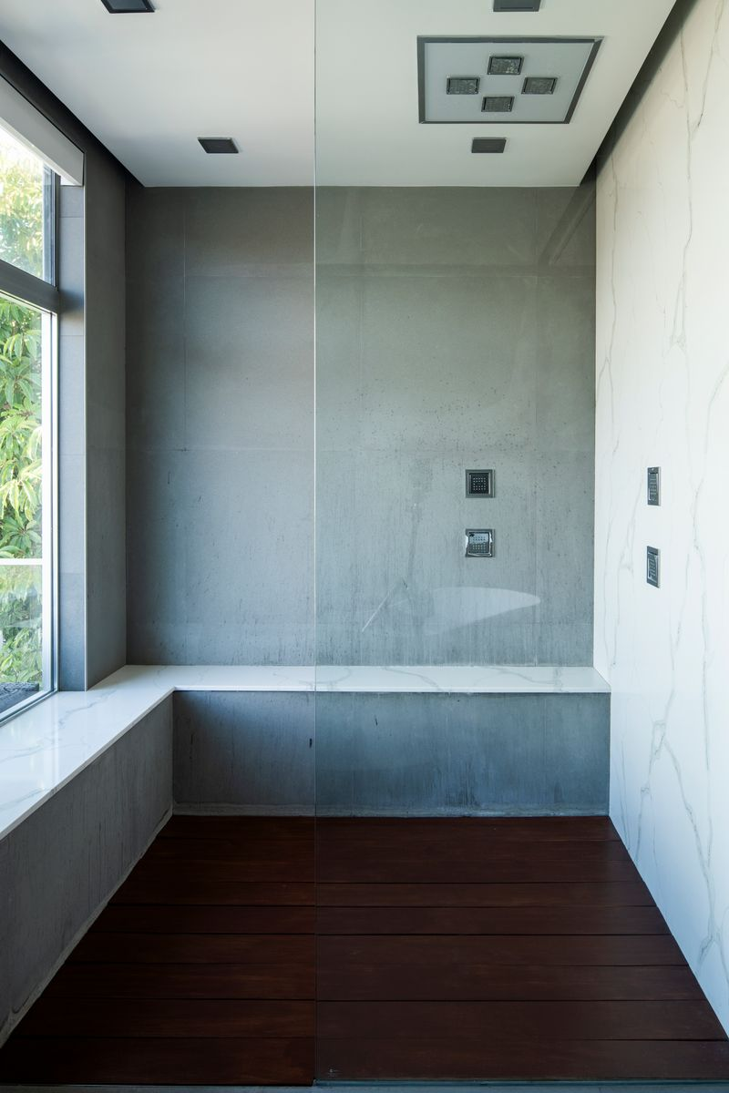 Next to the tub is a large walk-in shower enclosed in glass, featuring oversized gray wall panels, integrated bench seating, and rainfall fixtures.