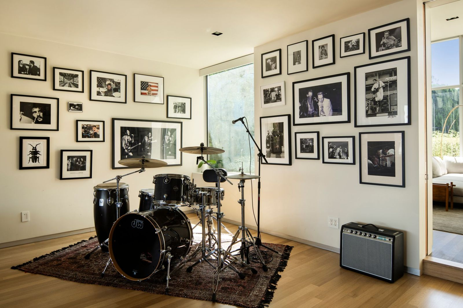 A full drum kit sits atop a patterned area rug, while an amplifier and microphone stand suggest the space is set up for both practice and recording.