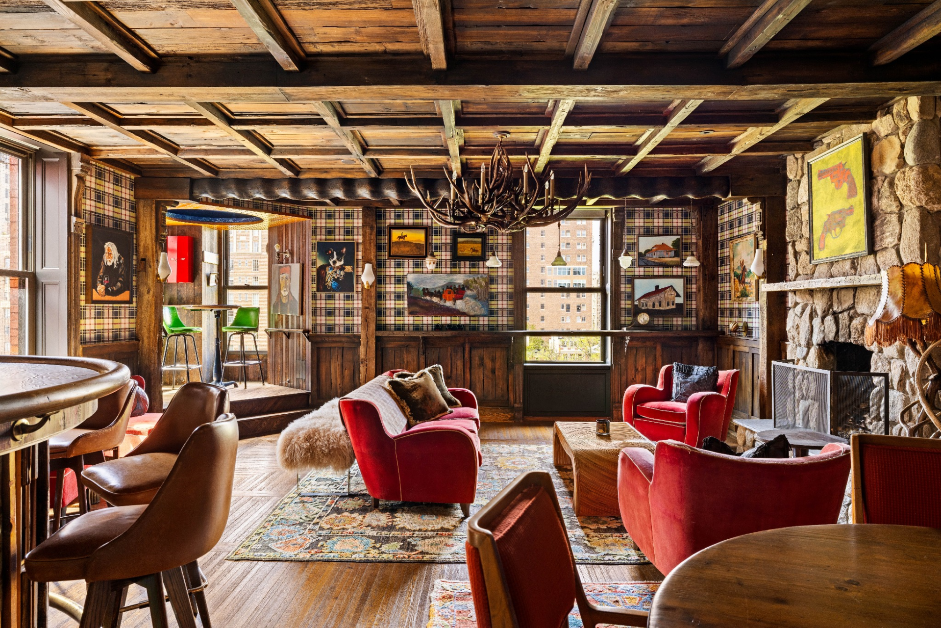 Inside, reclaimed wood beams, plaid wall coverings, and a stone fireplace create a layered, old-world vibe.