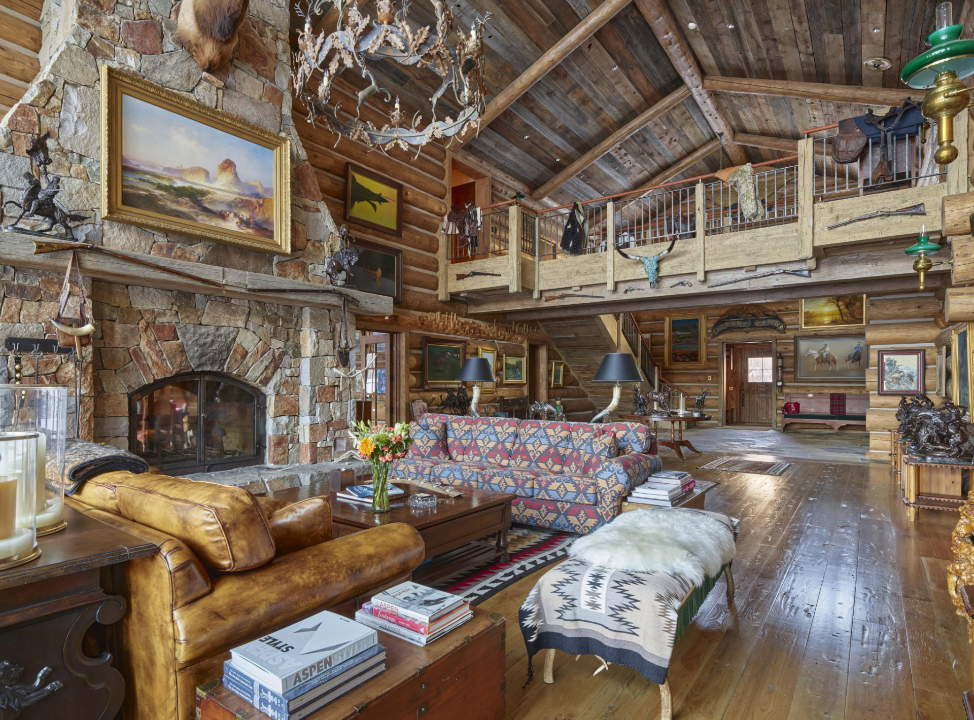 The seating area is arranged around the fireplace with leather sofas, patterned upholstery, and handcrafted wood furnishings, creating a natural gathering point within the room. 