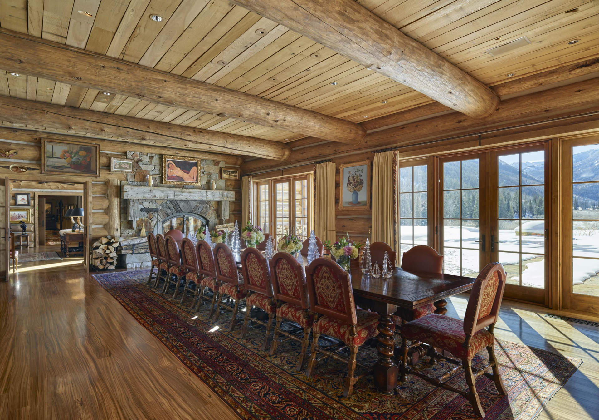 The formal dining area features a long dark wood dining table surrounded by high-backed upholstered chairs arranged to accommodate a large group. 