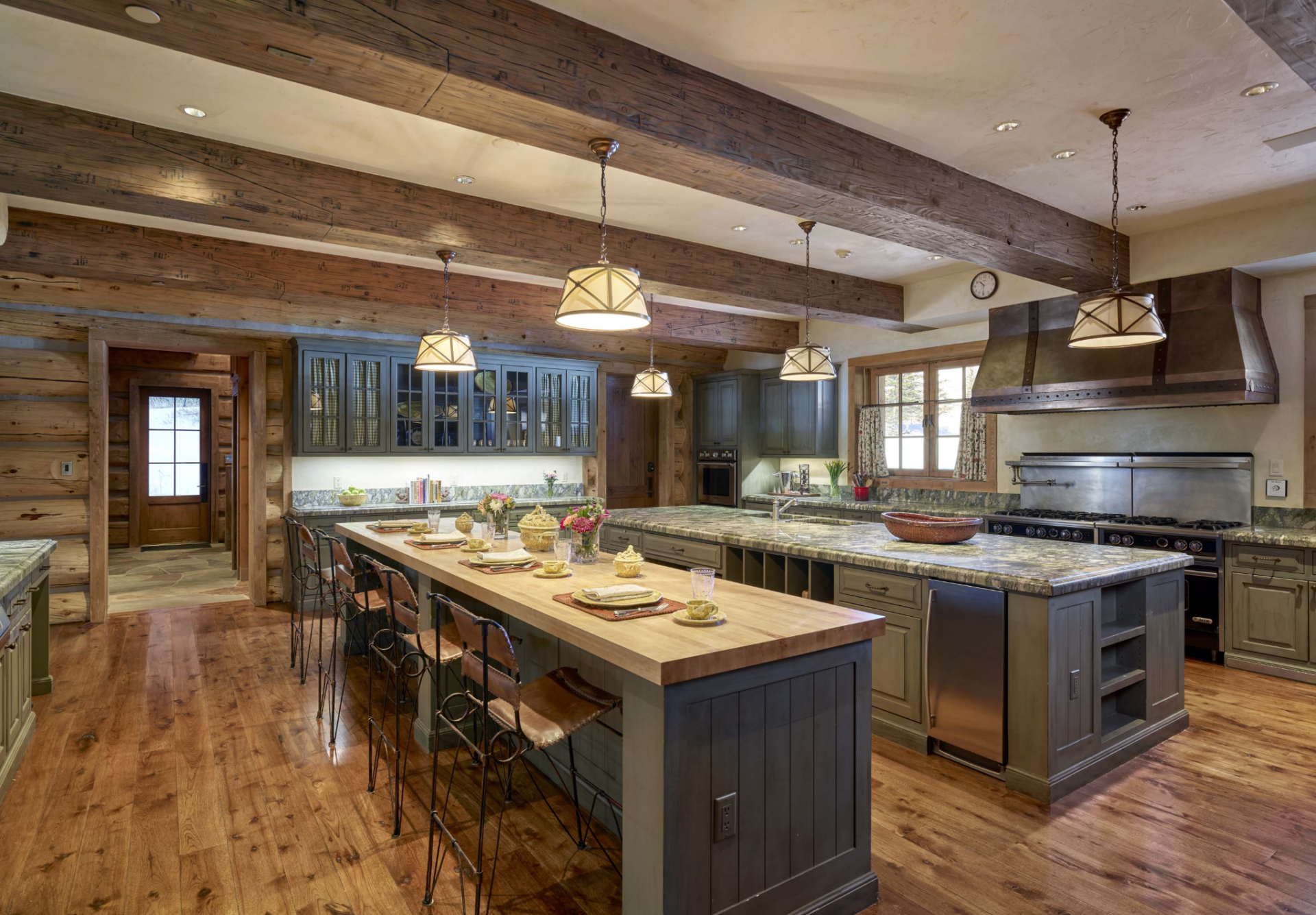 At the center are two oversized islands, one is topped with stone counters made for meal prep, while the second features a butcher-block surface with bar seating for casual meals. 