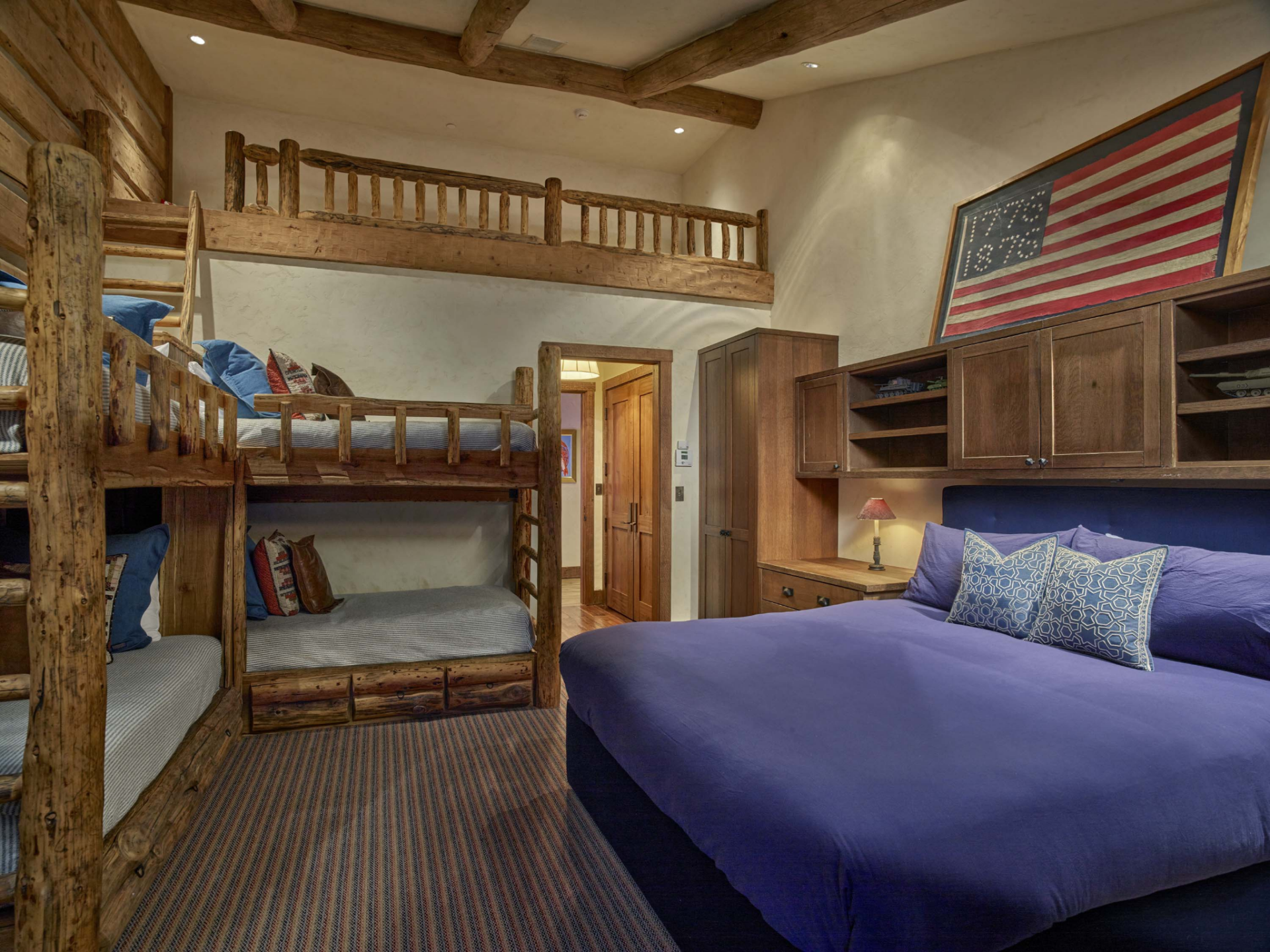 Multiple stacked bunks line one side of the room, while a larger bed is integrated into the opposite wall beneath custom cabinetry and shelving.