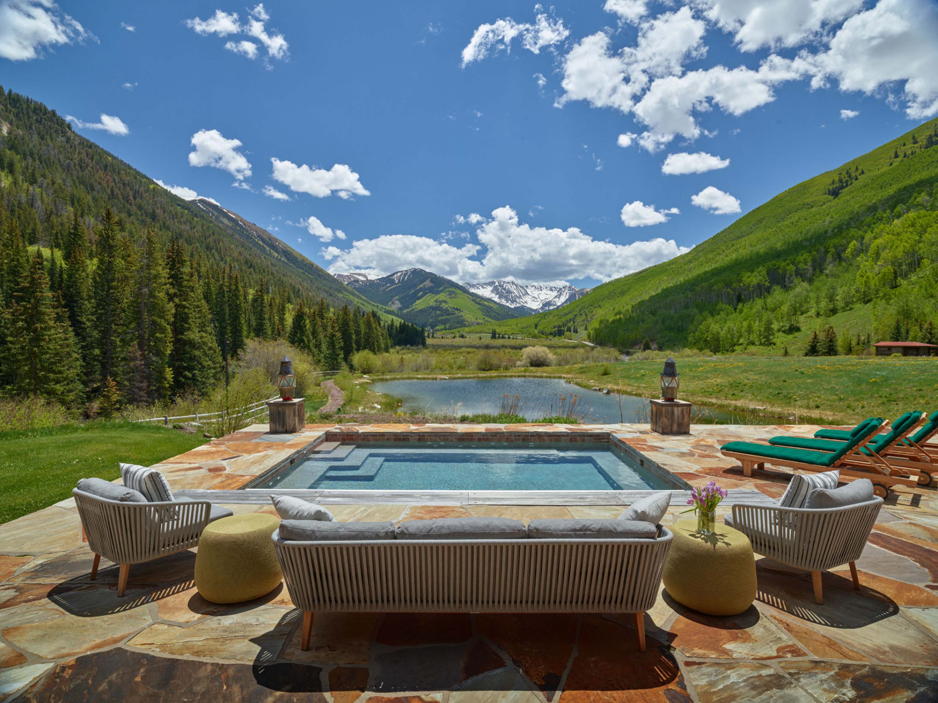 Set within a broad stone terrace, the spa is positioned directly in line with the valley, creating uninterrupted views across a pond, rolling meadows, dense forests, and the snow-capped peaks beyond.