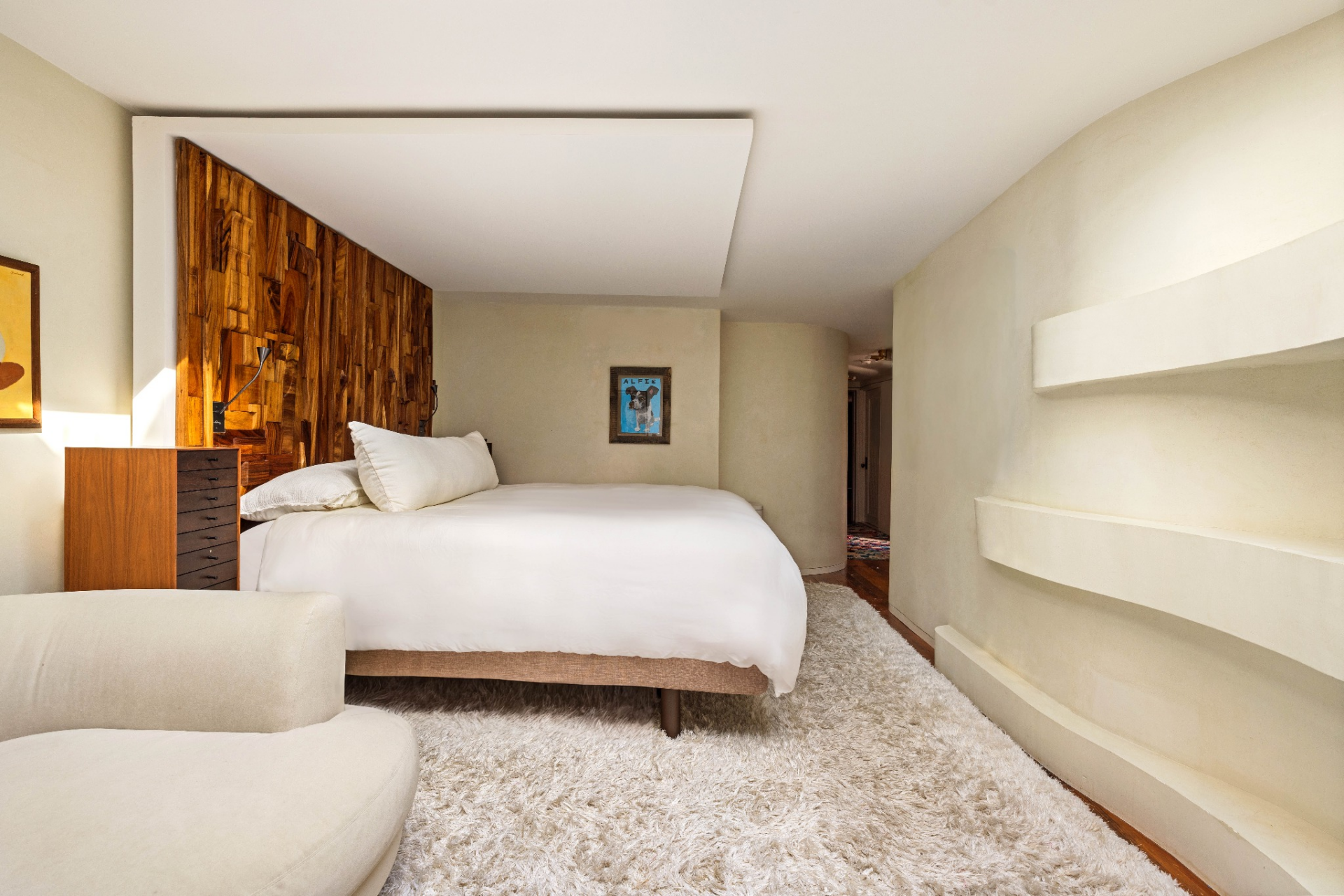 The bedroom itself is one of the home's most simple and modern-looking rooms, with soft plaster walls, a thick rug, and a sculptural wood accent wall framing the bed.