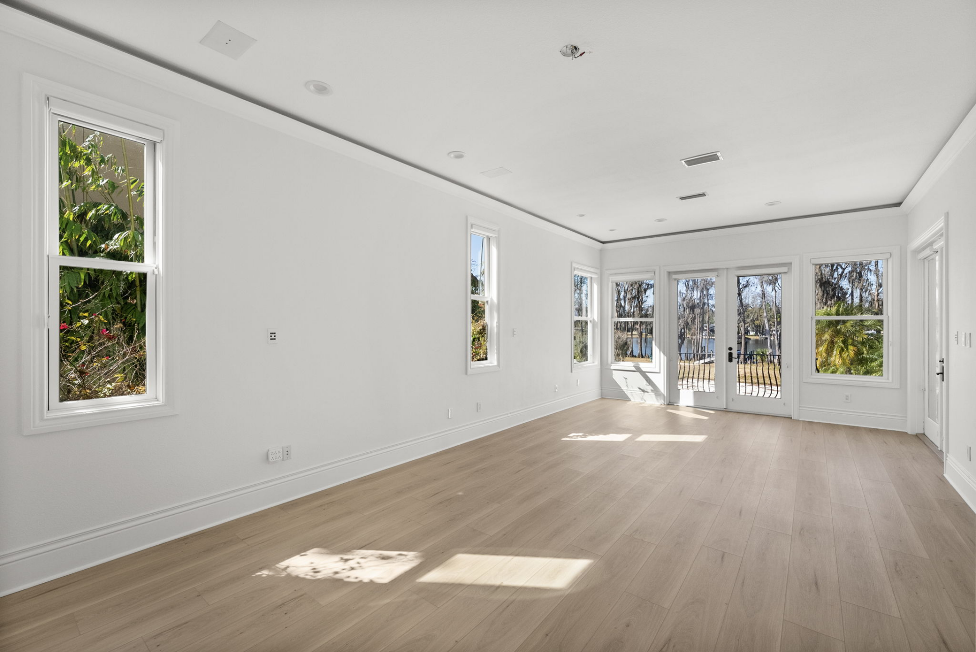 The bedroom is filled with natural light from multiple windows and French doors that open directly onto a private covered balcony overlooking the water.
