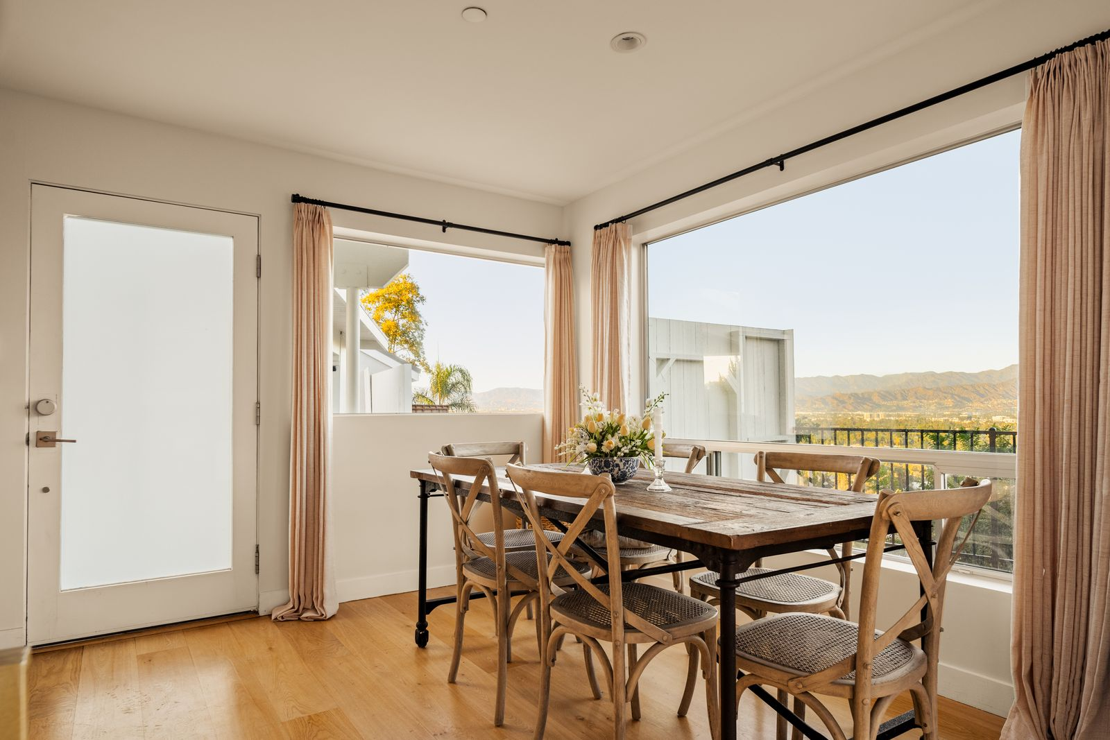Next to the great room, the dining area is positioned in a corner of oversized picture windows framed by soft pink curtains.