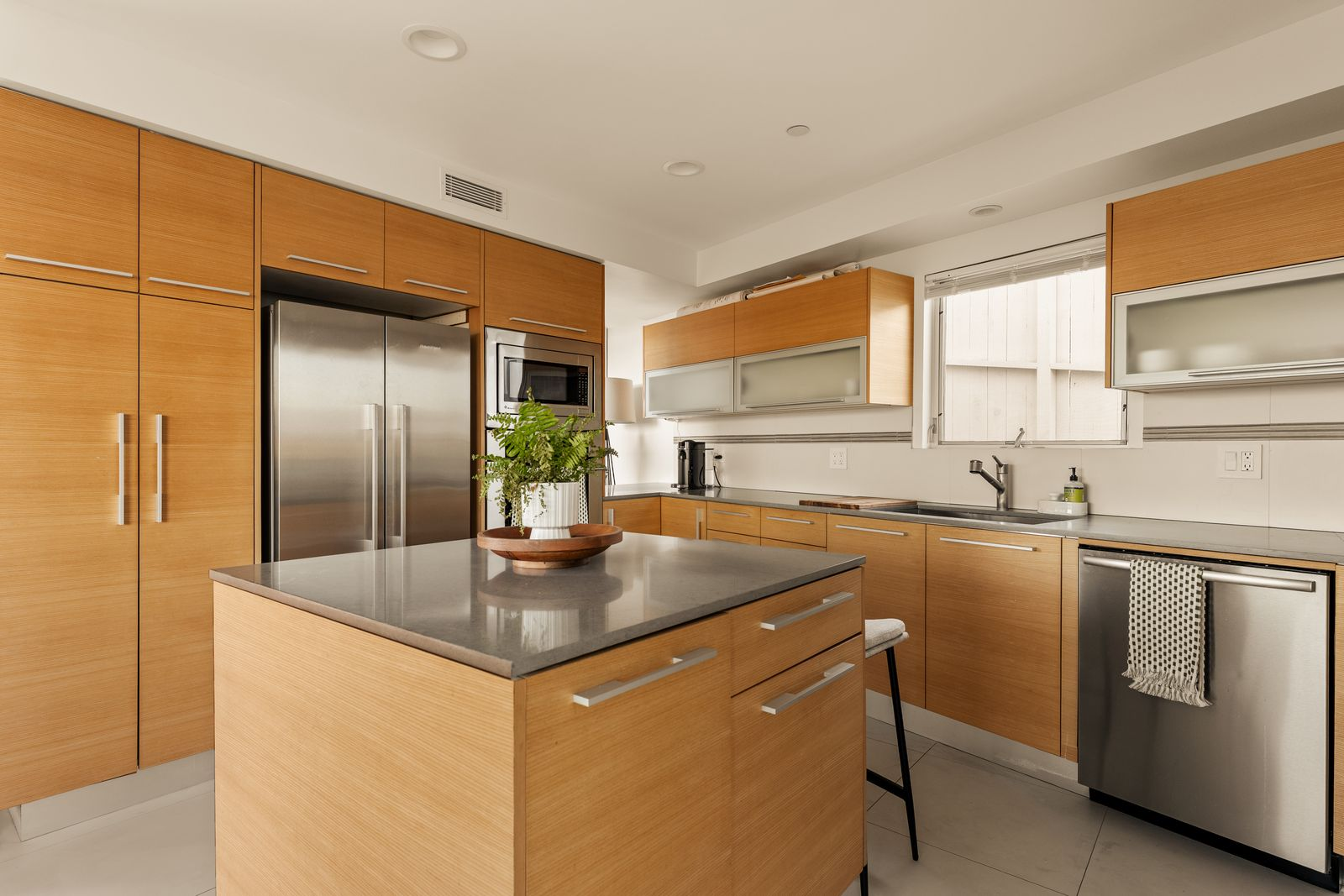 Floor-to-ceiling wood cabinetry wraps the room, concealing storage while framing a suite of premium stainless steel appliances, including a professional-grade gas cooktop beneath a sleek vent hood.