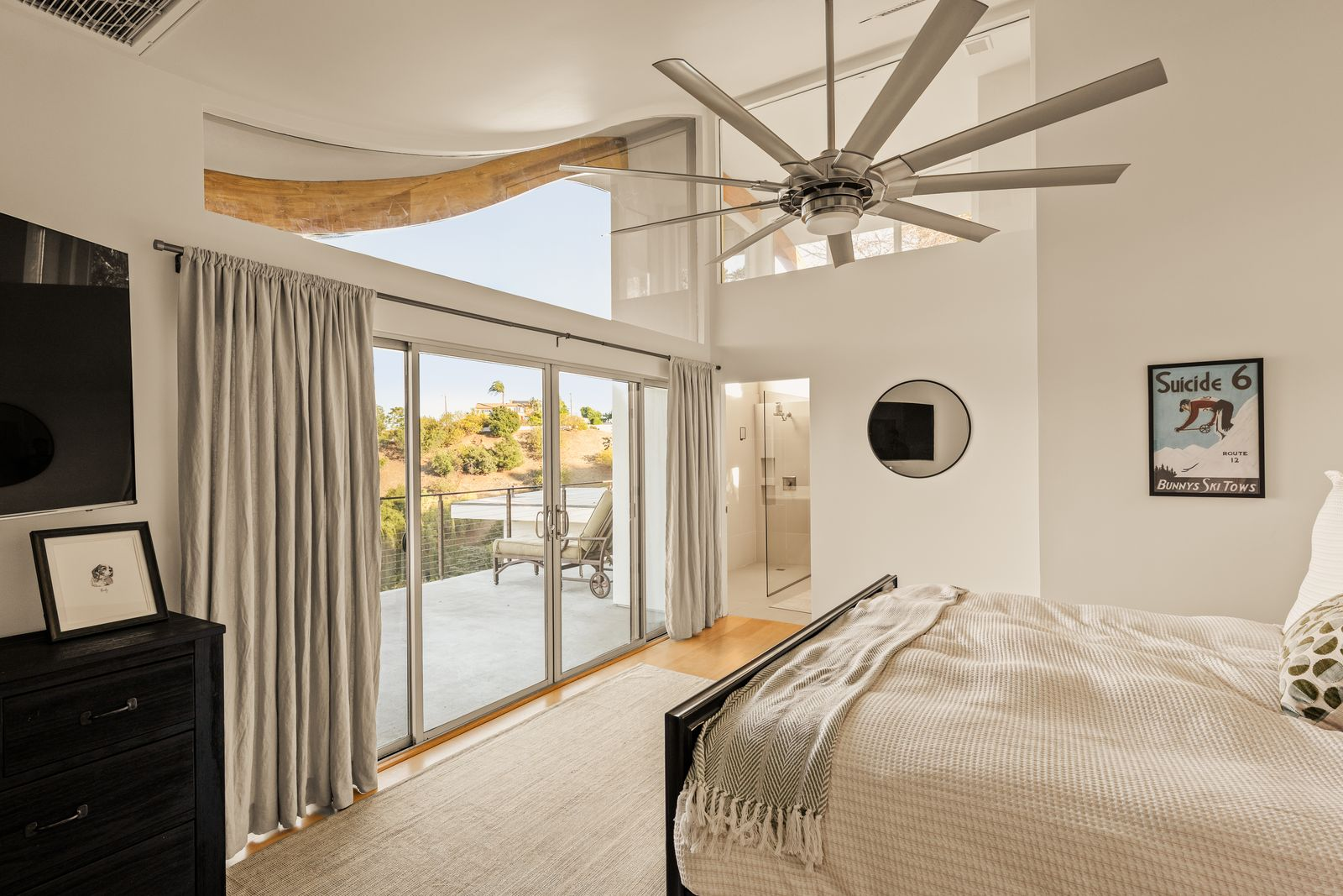 In the bedroom, a soaring ceiling rises above the sleeping area, while a dramatic curved wood beam draws the eye upward toward clerestory windows that bring natural light deep into the room. 