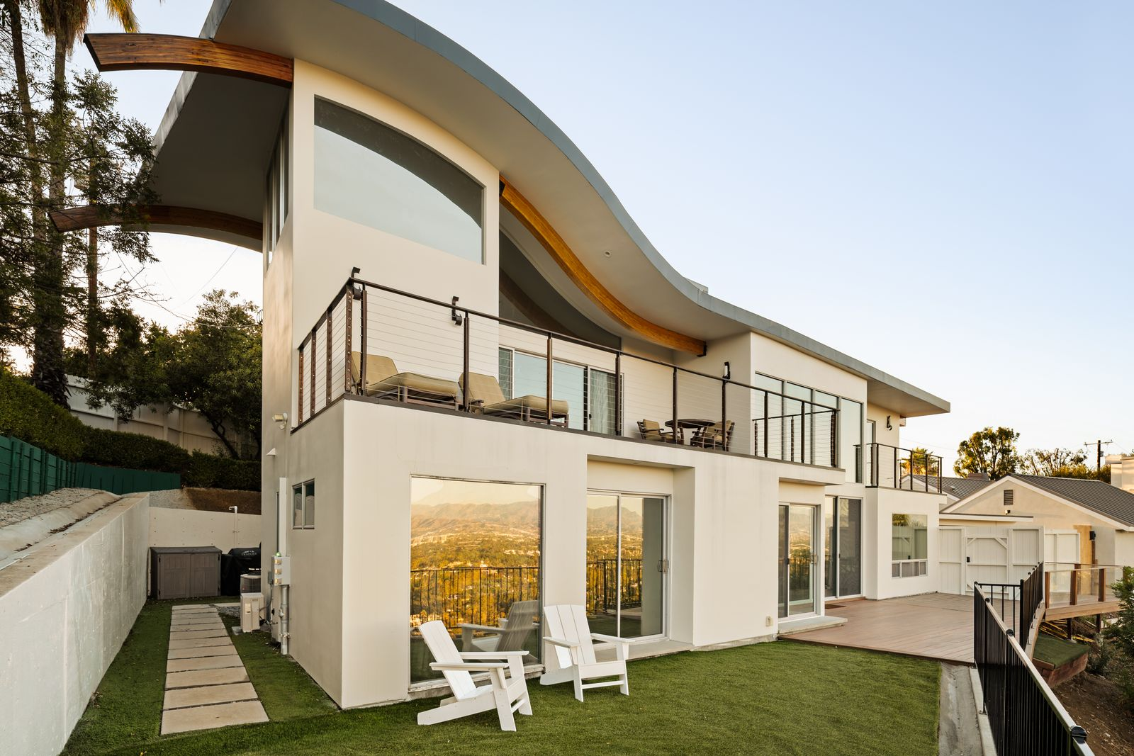 The main outdoor living area unfolds across a broad wraparound deck that stretches along the edge of the hillside finished with wide-plank decking and a landscaped turf terrace.