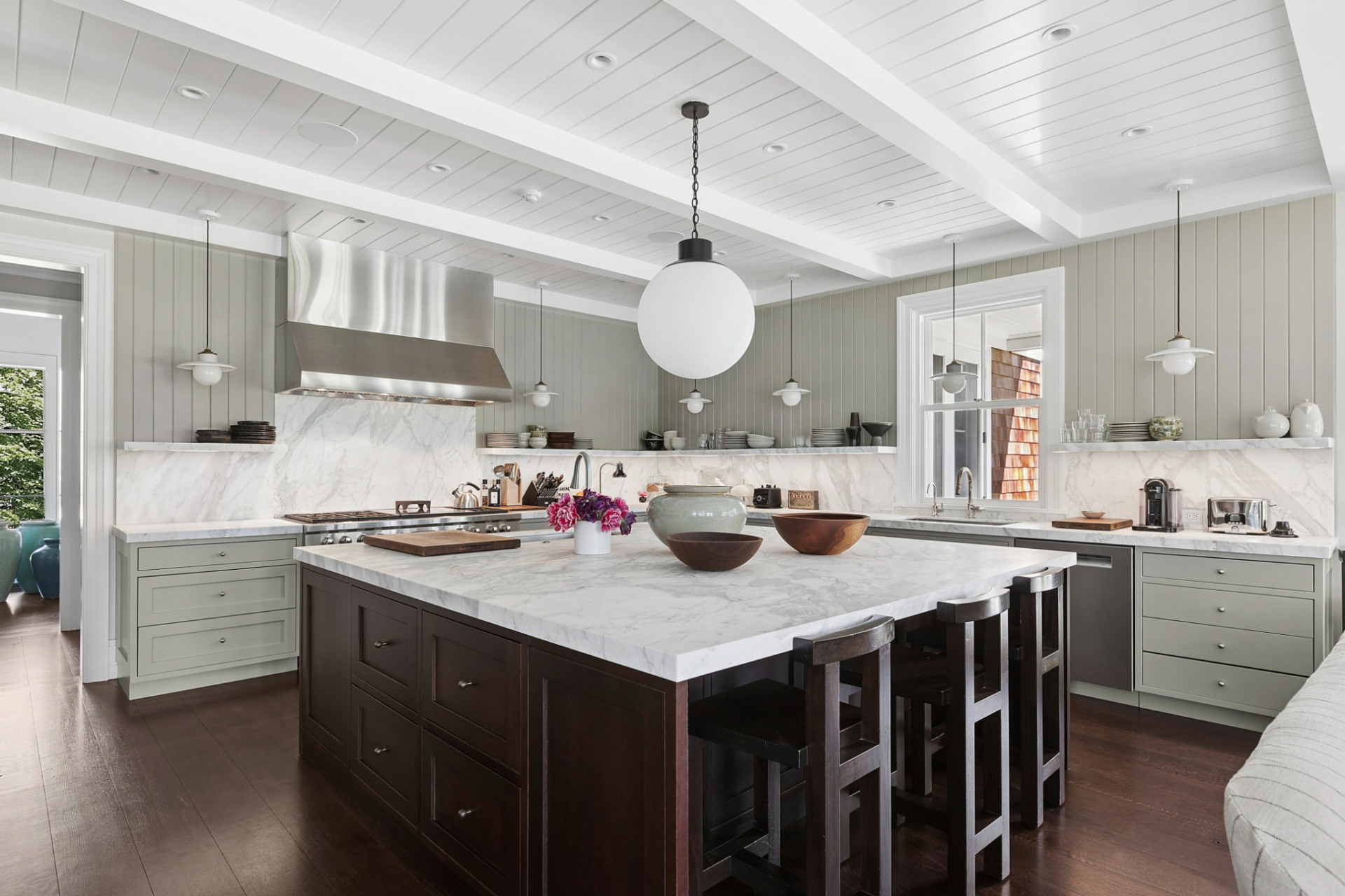 A professional-grade range sits beneath a stainless steel hood, and open display ledges wrap the perimeter, providing space for everyday dishware and decorative accents around the island.