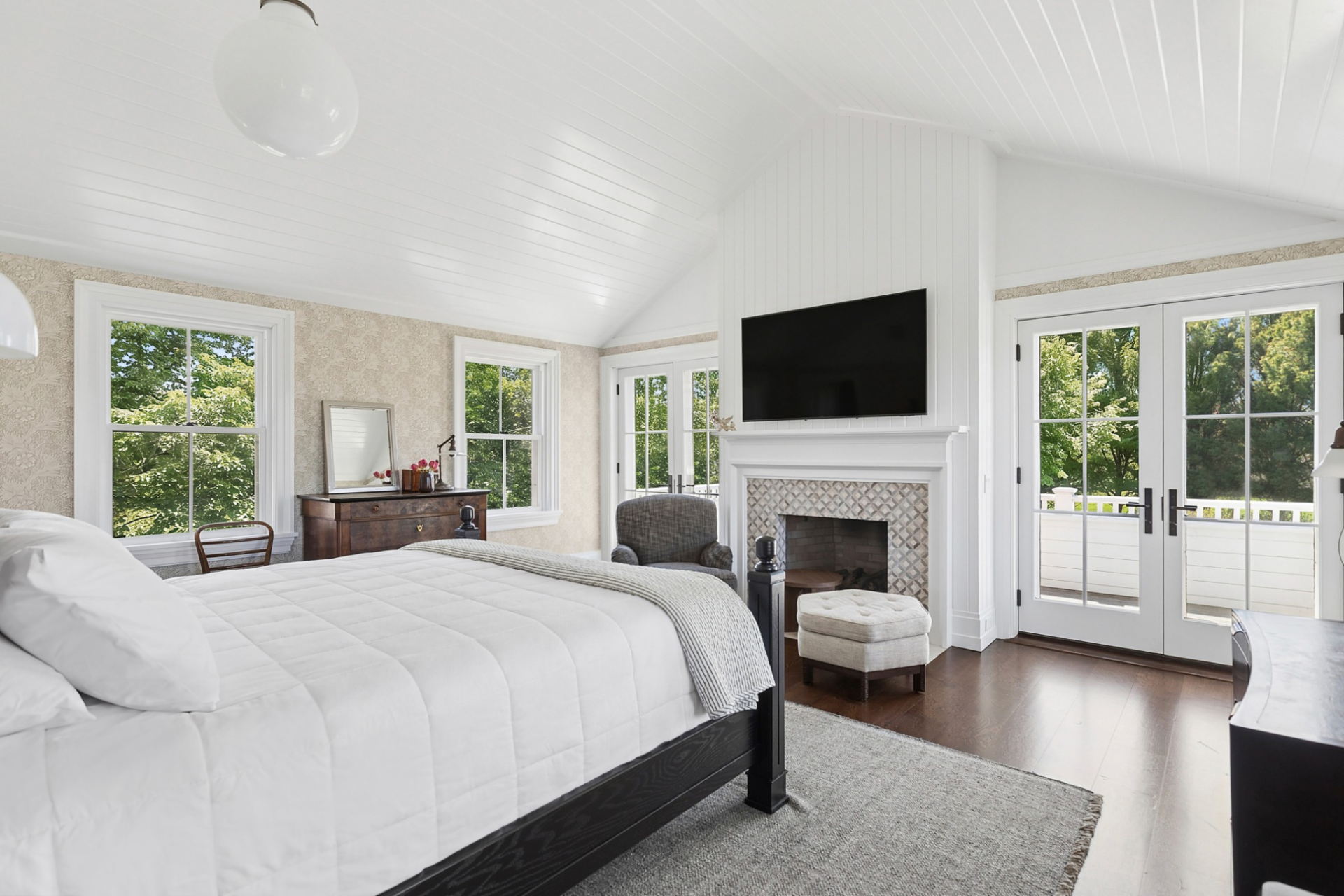 Patterned wall coverings, dark-stained hardwood floors, and oversized windows create a classic Hamptons look, while French doors beside the fireplace open to a private balcony overlooking the property.