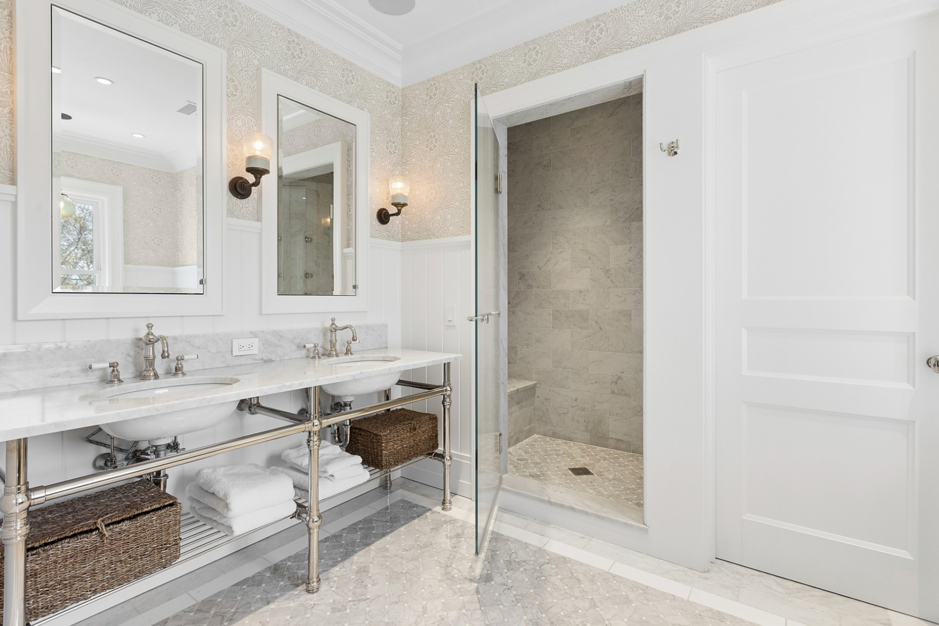 The connected bathroom continues the timeless design with marble floors, marble shower walls, and a double vanity topped with matching stone counters.