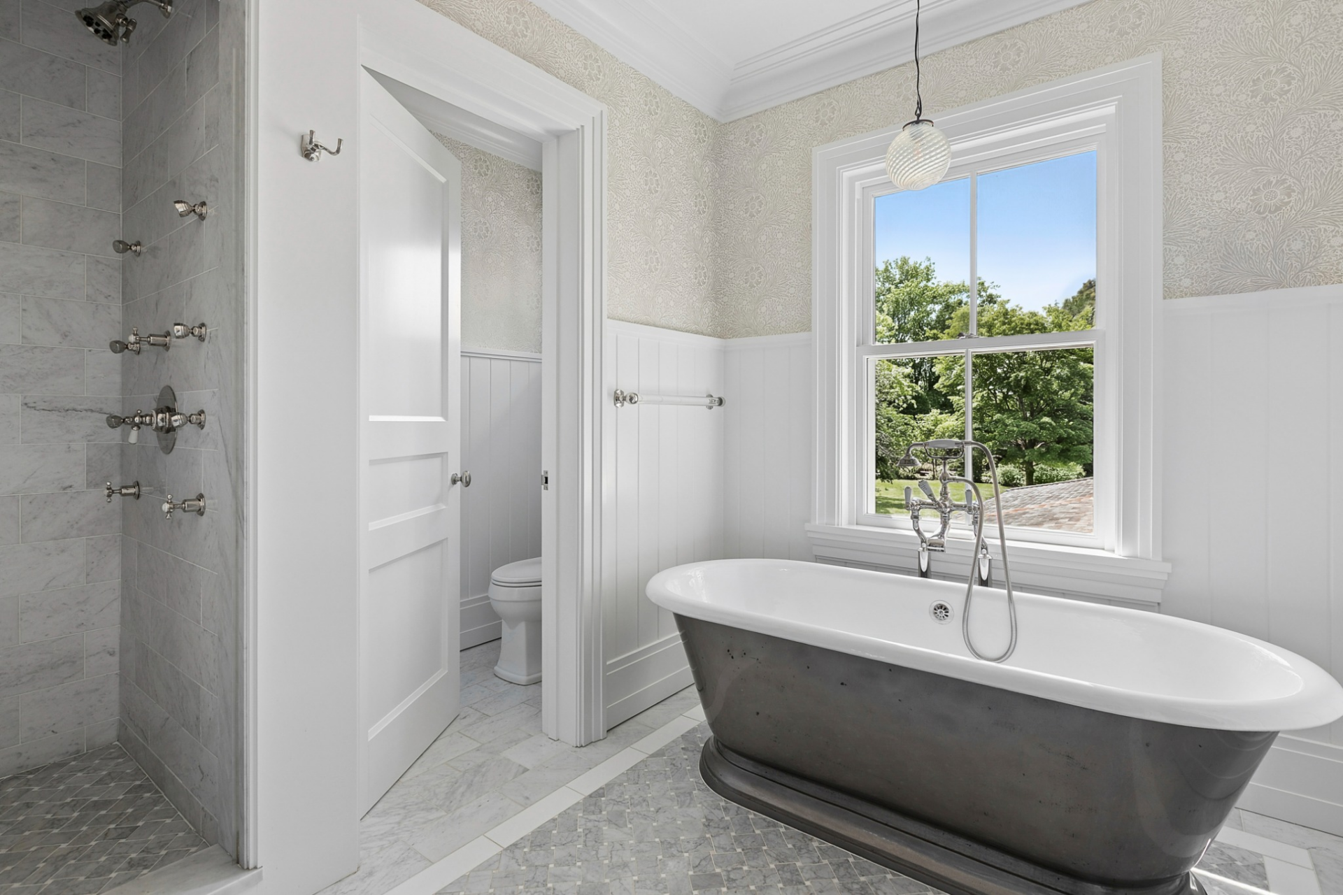 Across the room, a freestanding soaking tub sits beneath a large window overlooking the grounds, while a separate water closet completes the space.