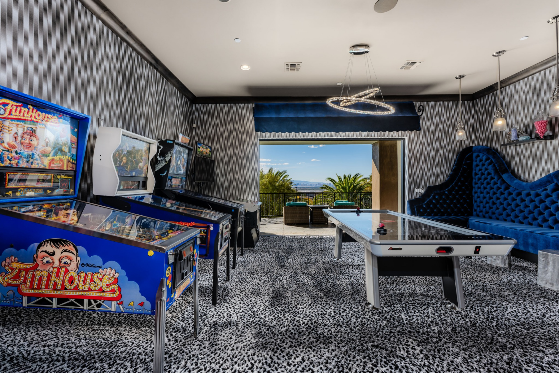 For recreation, the home includes a dedicated game room outfitted with vintage arcade machines, an air hockey table, and blue velvet lounge seating.