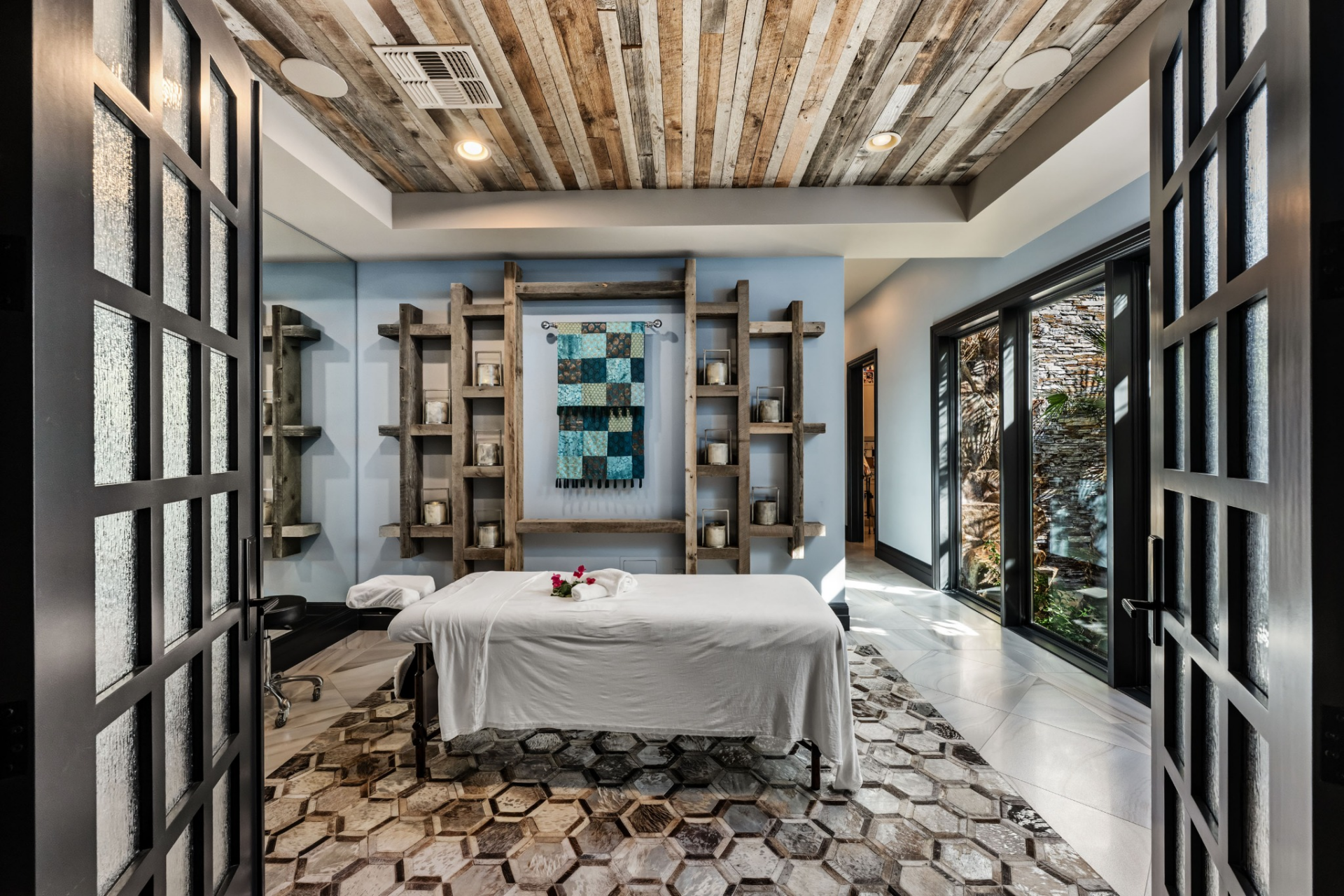 The home also has an abundance of wellness amenities, including a private massage room where rustic wood accents, custom shelving, and floor-to-ceiling glass bring natural elements into the space.