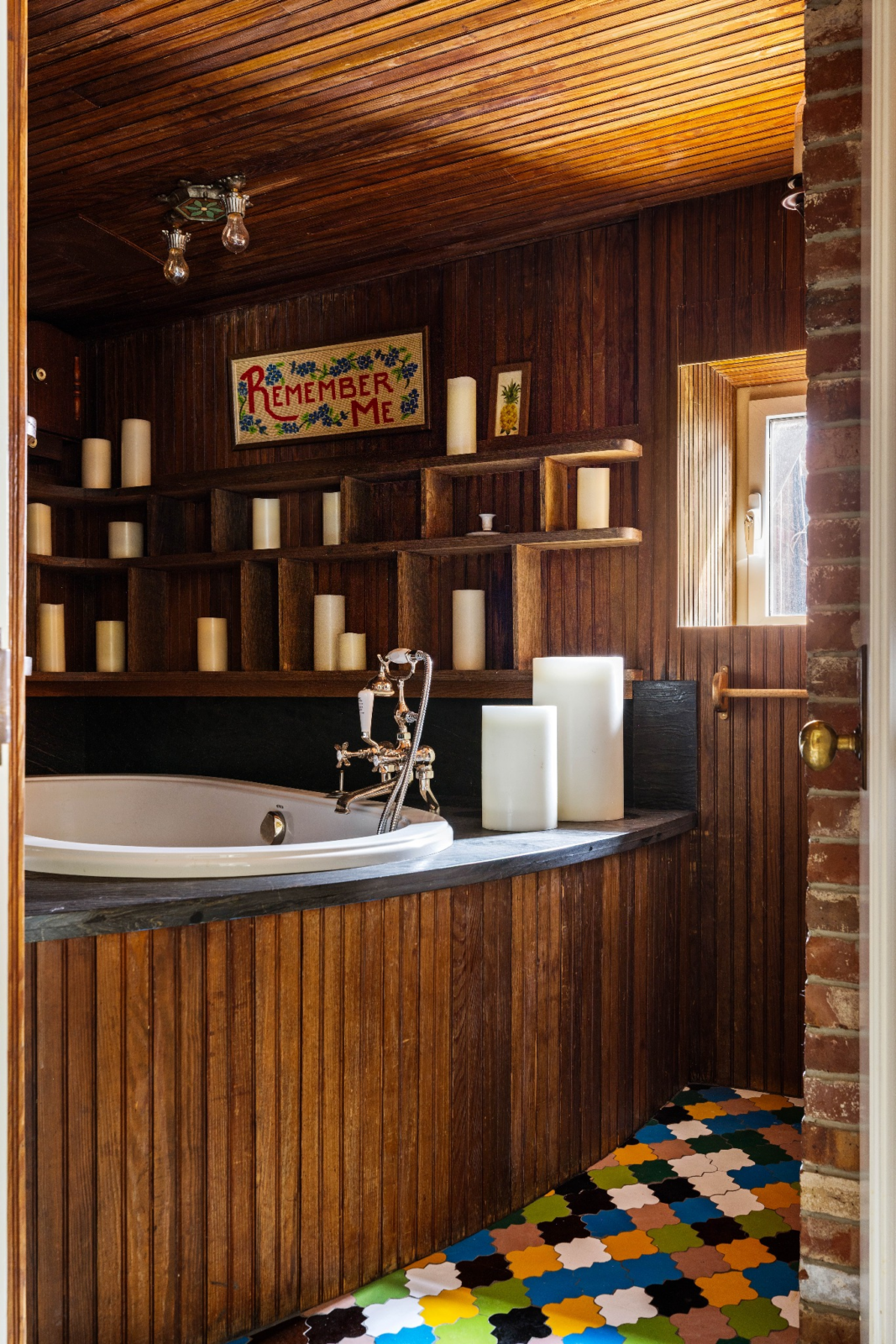 Beyond the main bathroom is a dedicated soaking room where a built-in tub is lined in rich wood paneling from floor to ceiling and surrounded by tall cream-colored candles.