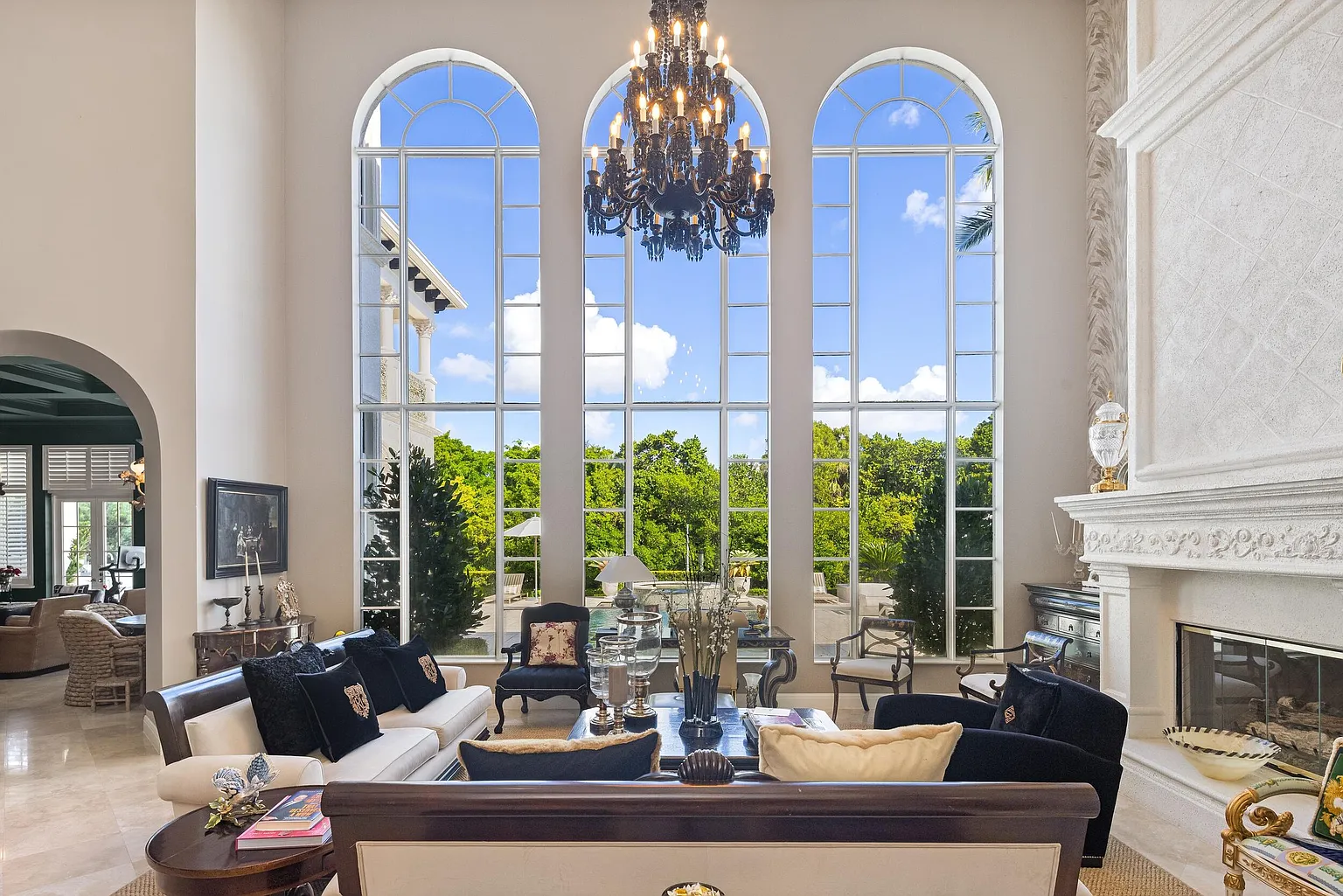 The home opens into a dramatic double-height living room with a carved fireplace and framed by towering arched windows. 
