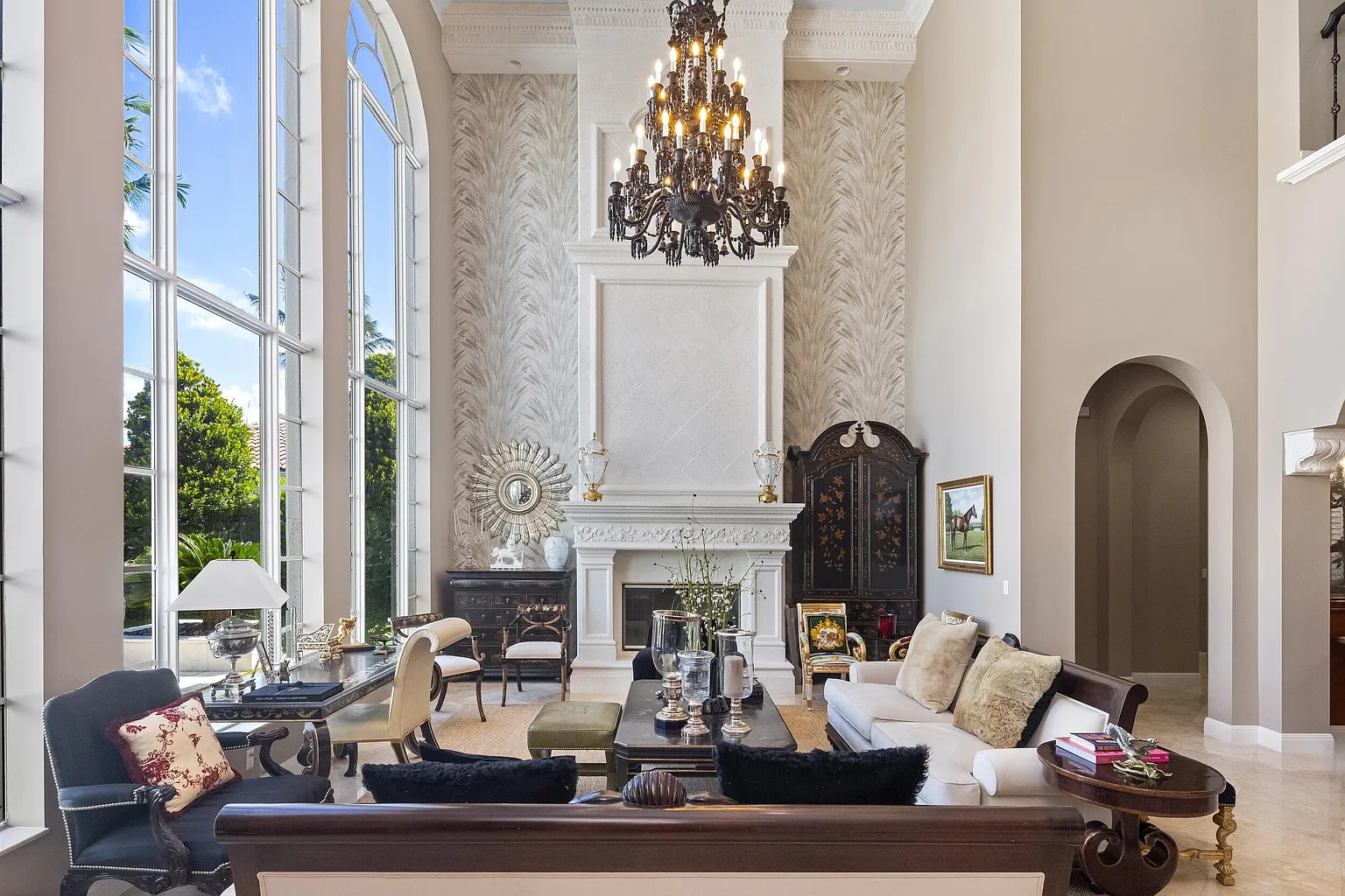 A grand black crystal chandelier hangs from the soaring ceiling, reinforcing the room’s sense of scale and serving as a centering point above the formal seating arrangement.