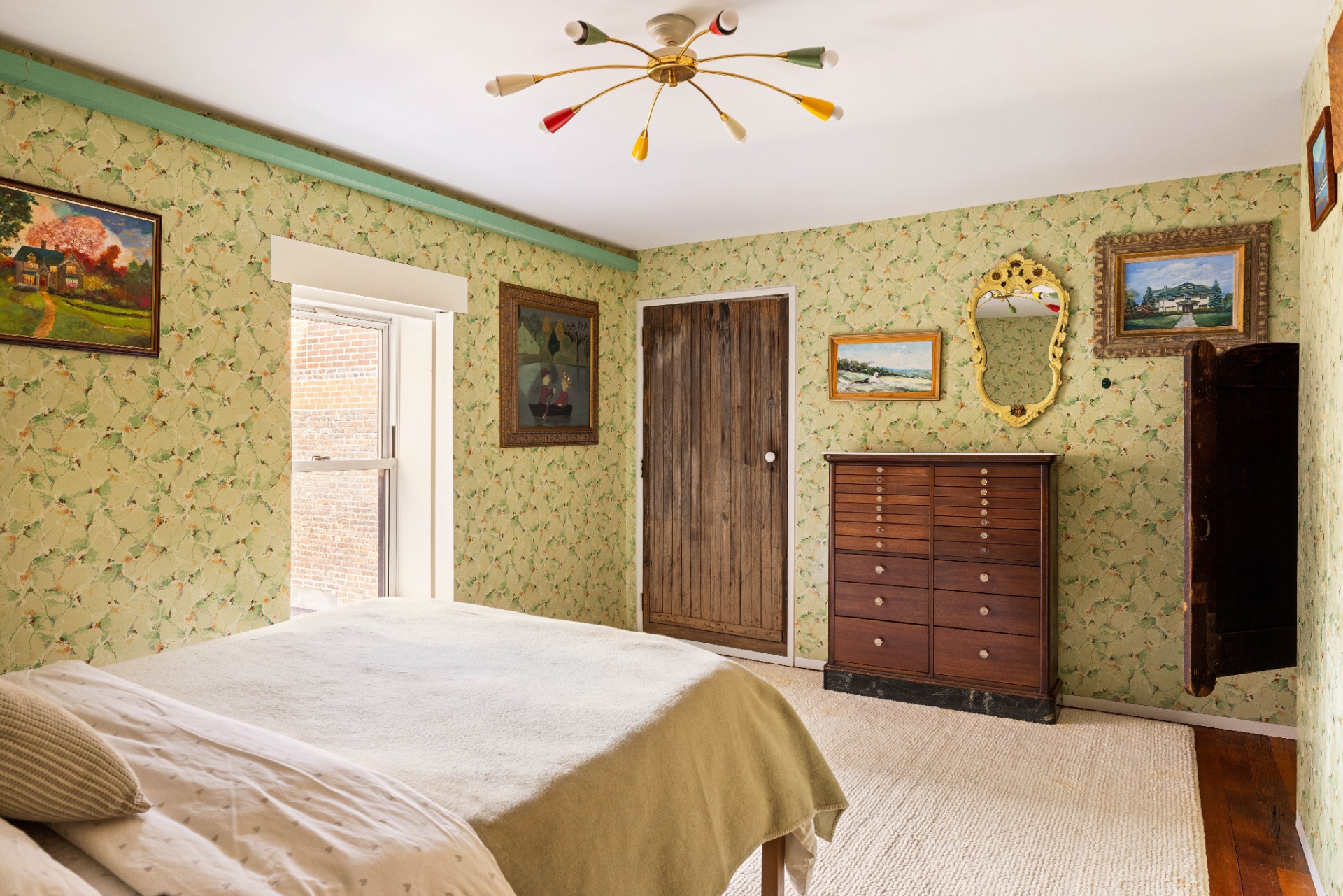 Framed artwork, a decorative mirror, and a midcentury-style light fixture add personality without overwhelming the space, while the warm wood door and dresser provide contrast against the patterned walls.