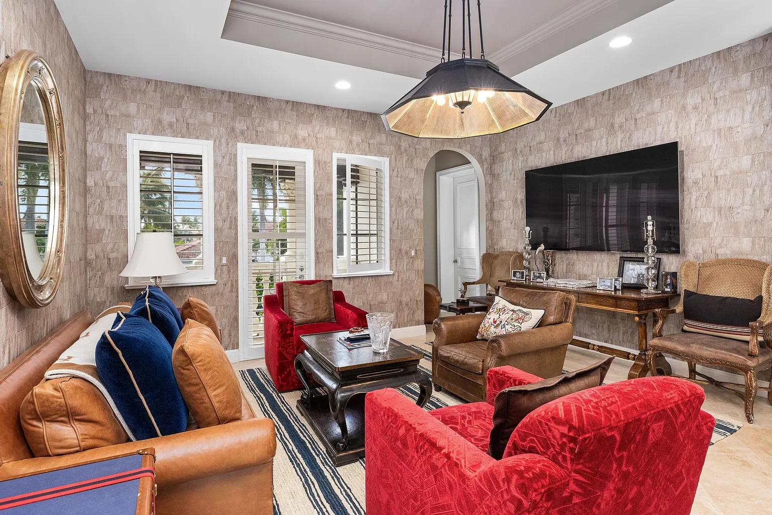 The room is centered around a wall-mounted television, with a mix of leather seating and plush accent chairs arranged around a dark wood coffee table.