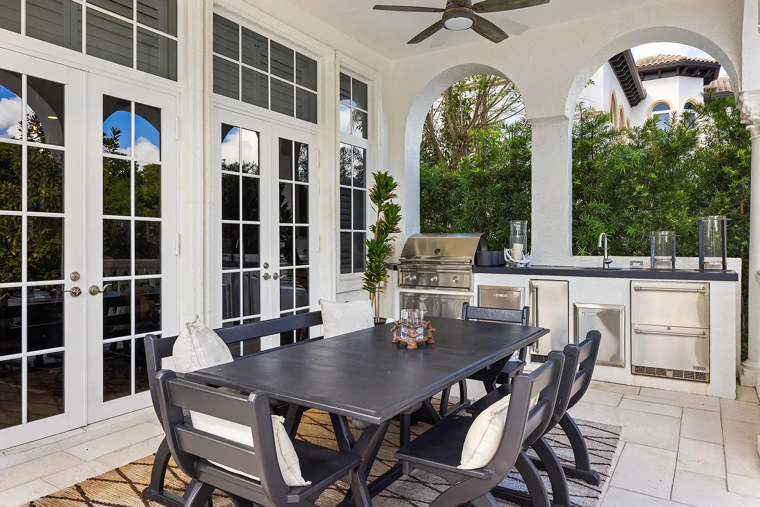 A built-in summer kitchen is fully equipped for outdoor cooking, with a grill, sink, refrigeration, and generous counter space positioned beside a dining table.